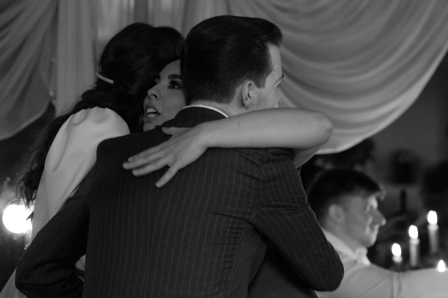 A couple embraces on a dance floor at an elegant event with candlelit ambiance in black and white.