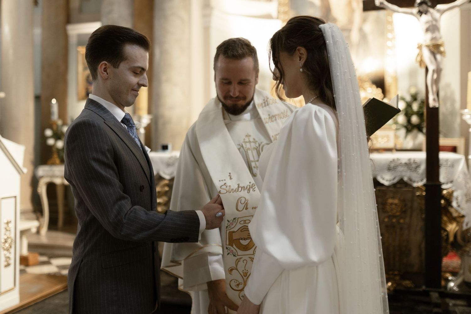 A couple stands at the altar during their wedding ceremony with an officiant in ornate religious robes.