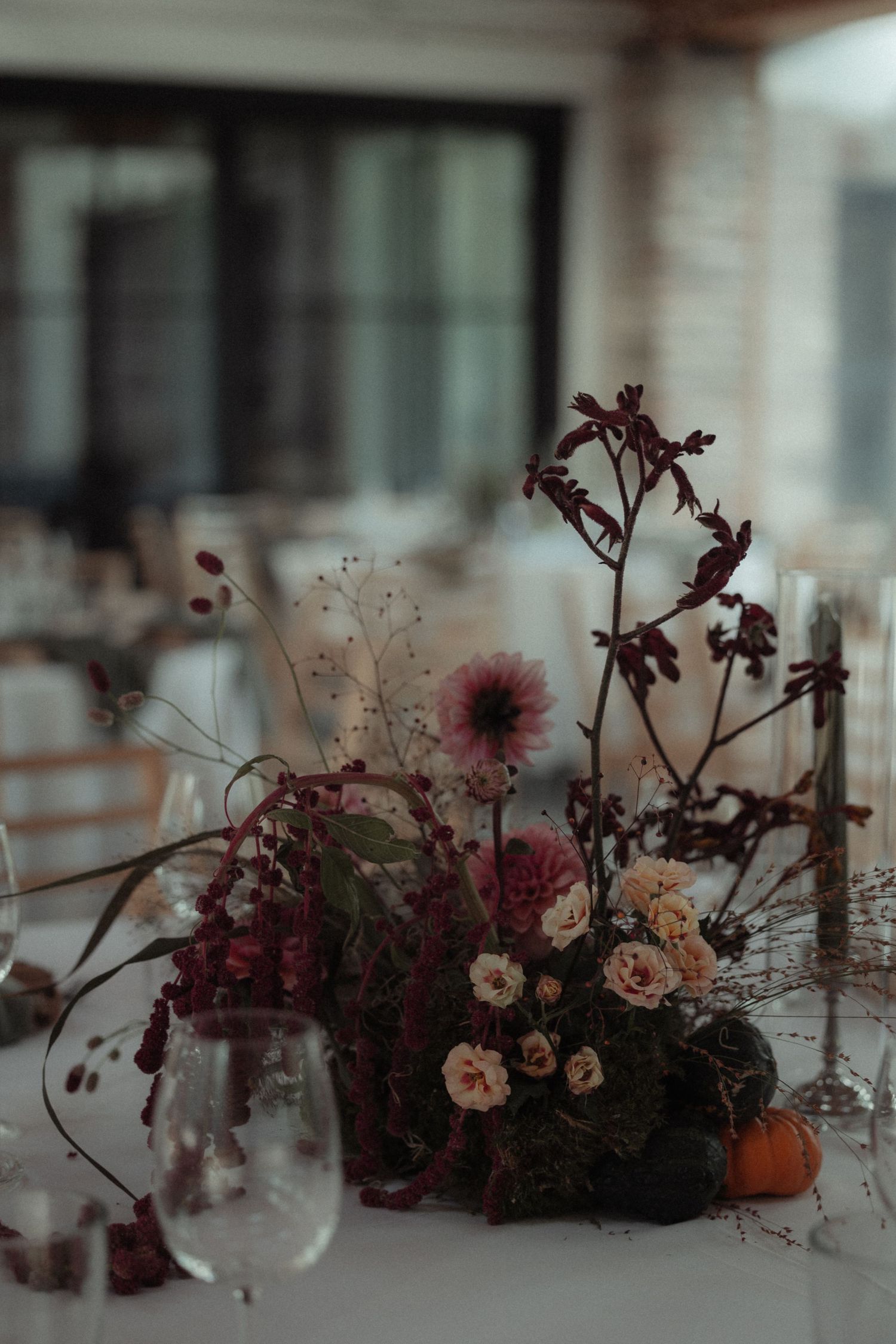 Moody floral centerpieces with burgundy and peach blooms arranged in a romantic style on a white tablecloth.