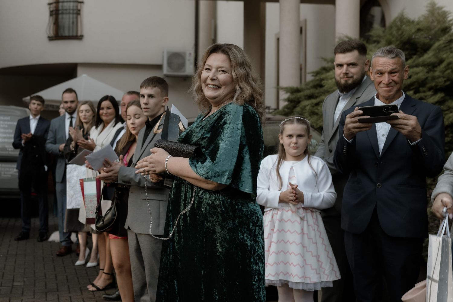 A group of wedding guests stand together in formal attire, with emerald green and dark suits creating an elegant scene.