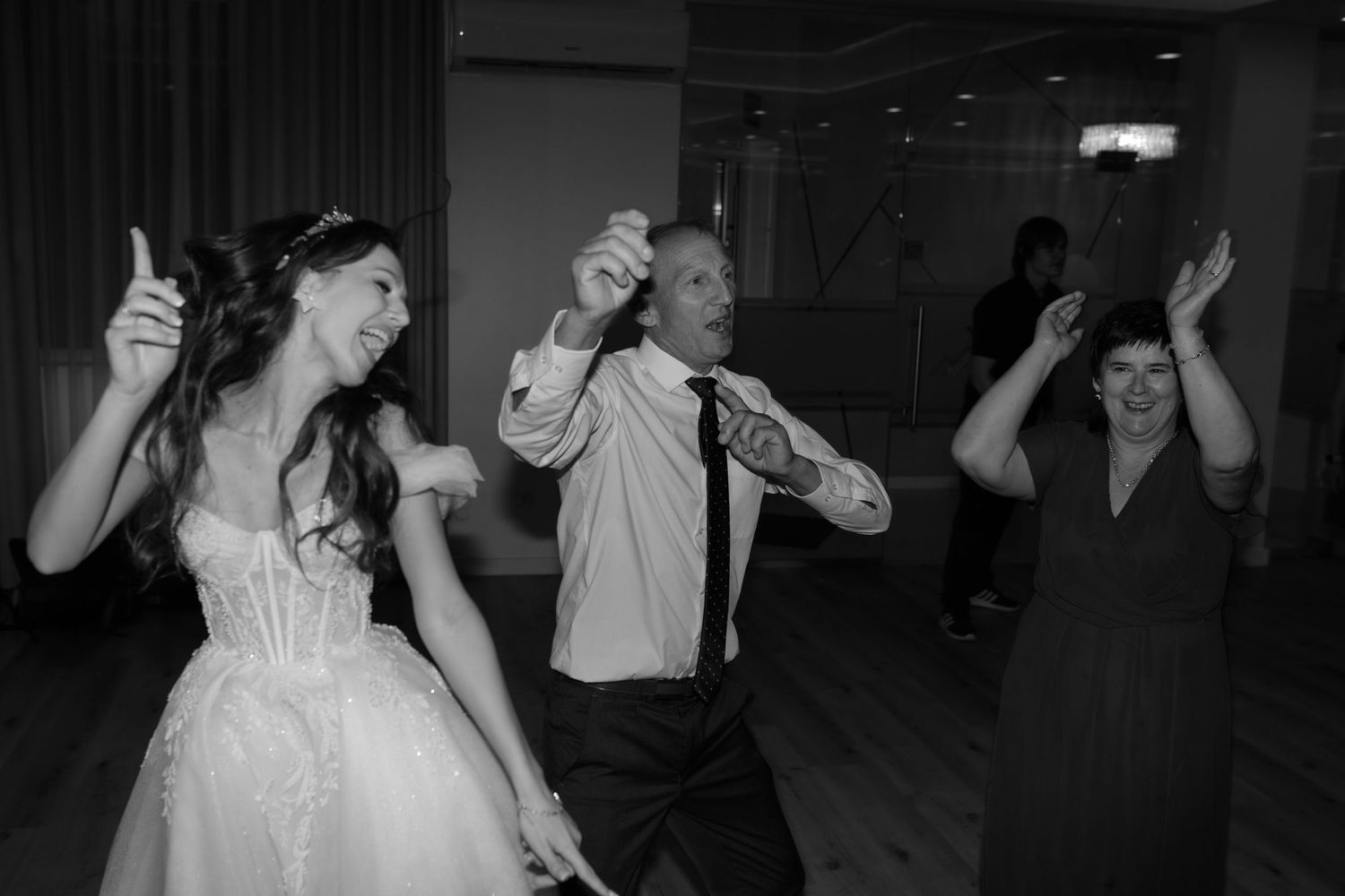 Black and white photo of wedding reception guests dancing energetically on the dance floor at night.