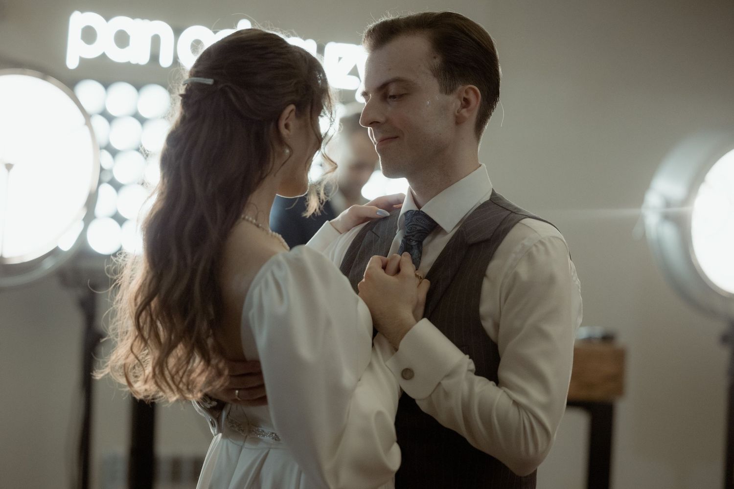 A romantic couple dances together intimately in a dimly lit room with illuminated signs in the background.