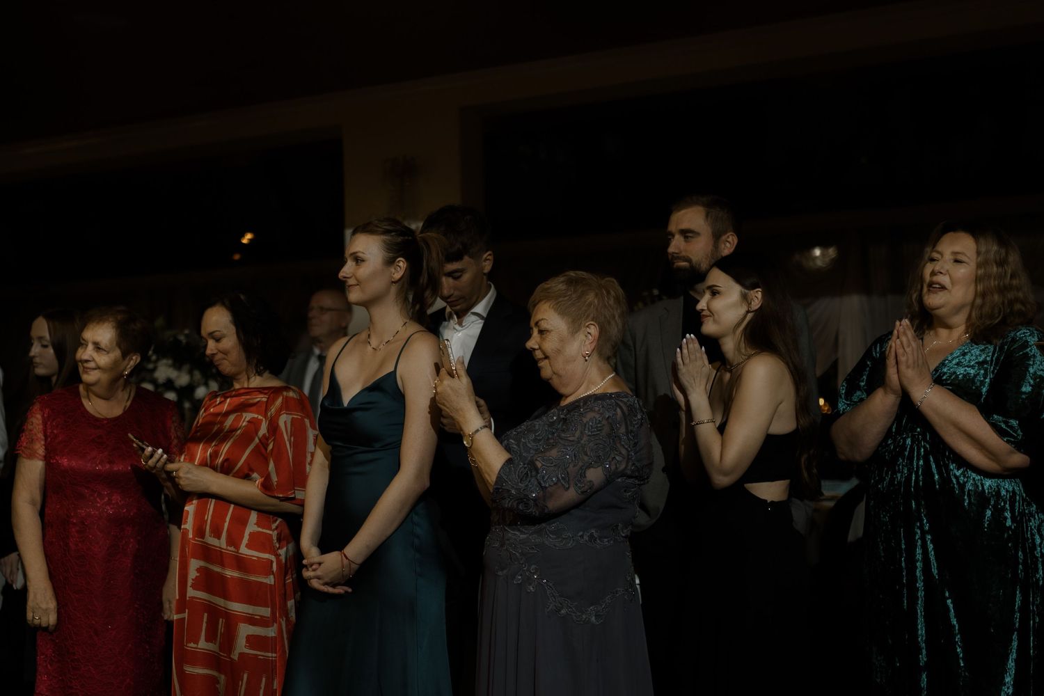 A lineup of people standing together in formal attire during a dimly lit evening event.
