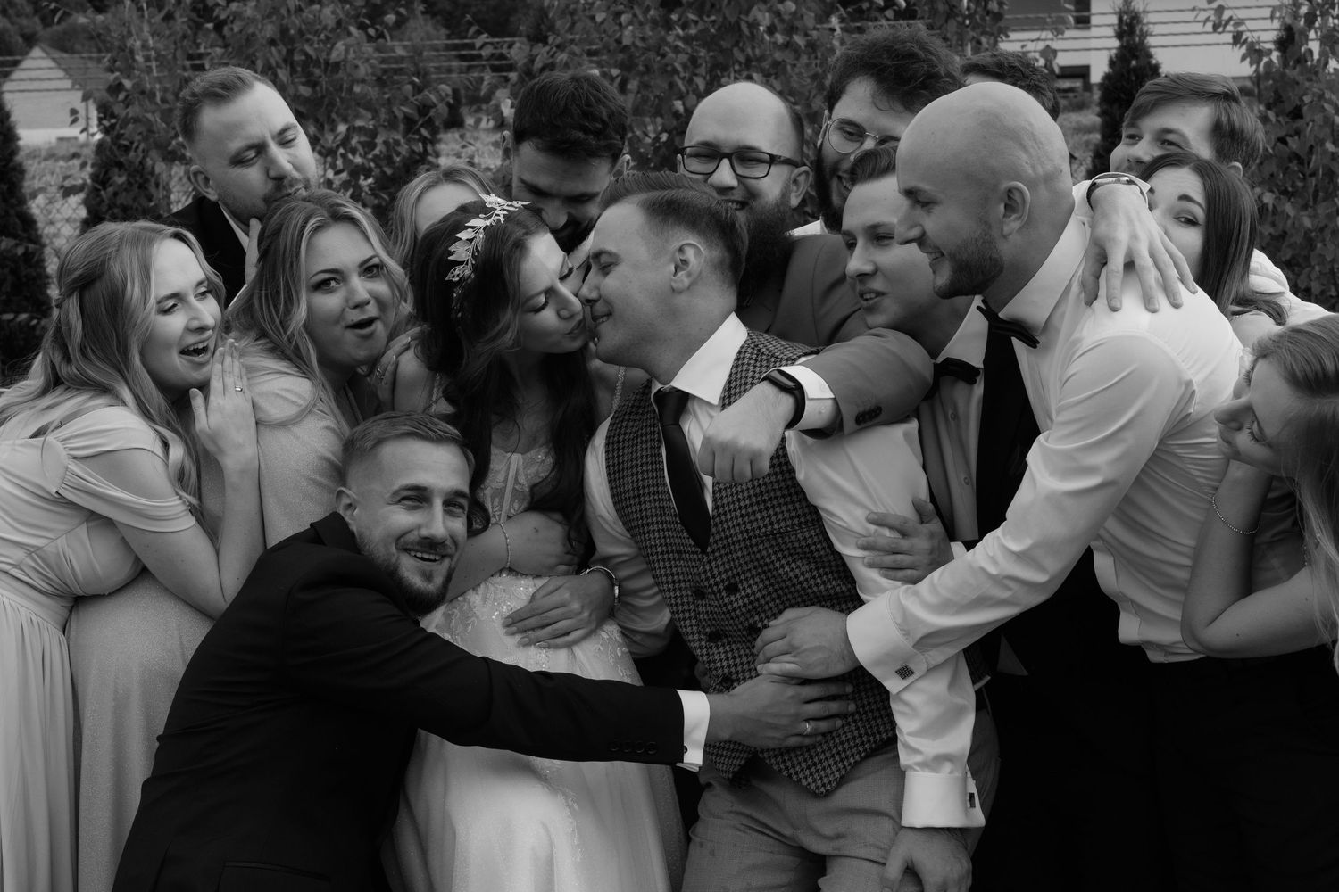 A joyful wedding party gathers closely together for a candid black and white group photo in celebration.