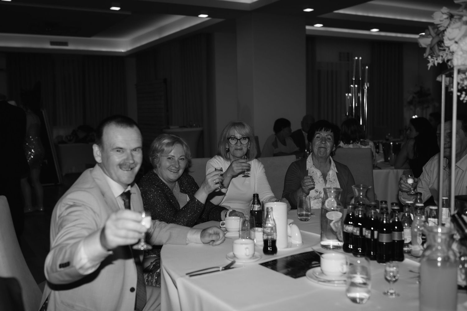 A group of people seated at a dining table with drinks and bottles during what appears to be a social gathering.