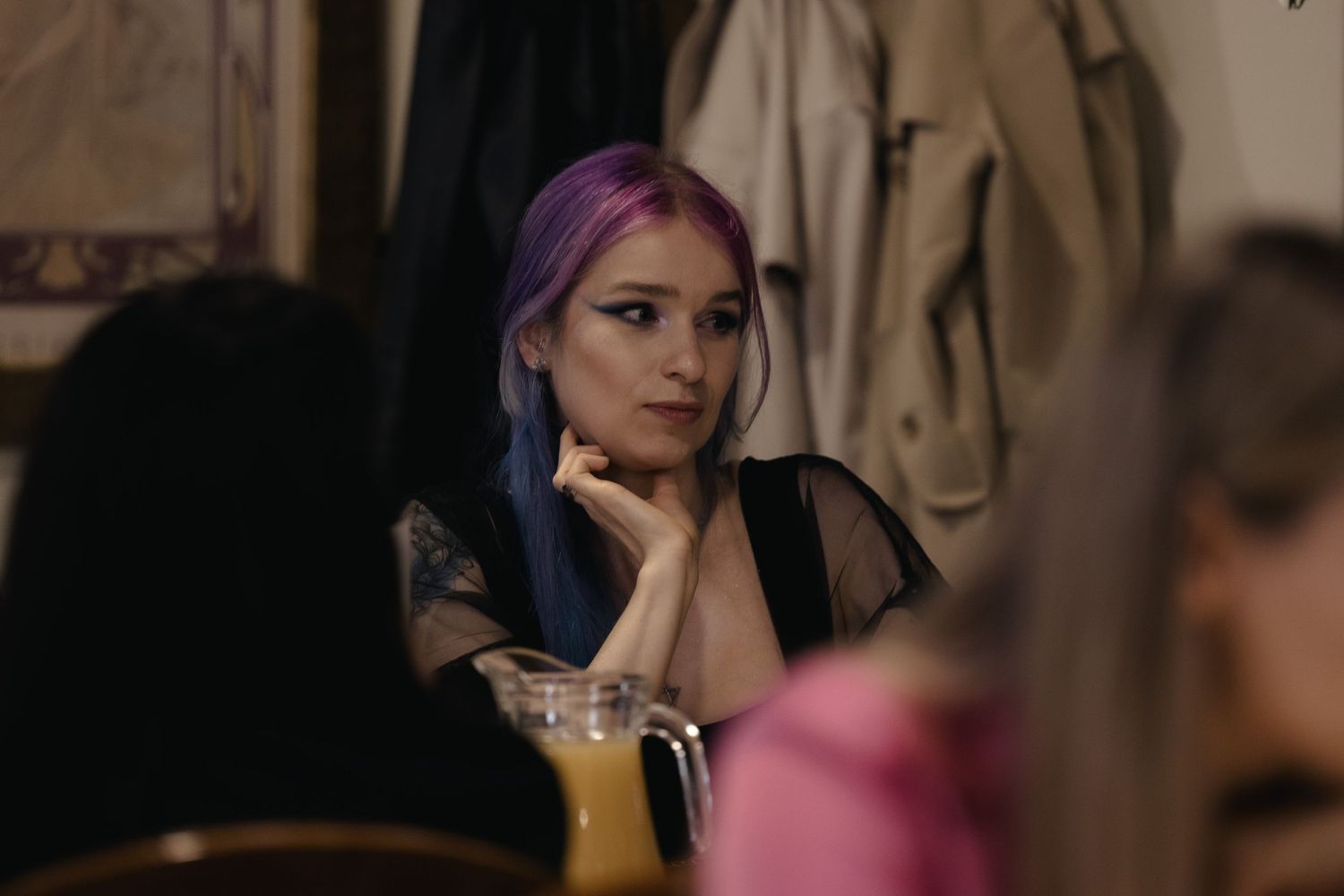 A person with vibrant purple hair sits thoughtfully in a dimly lit room.
