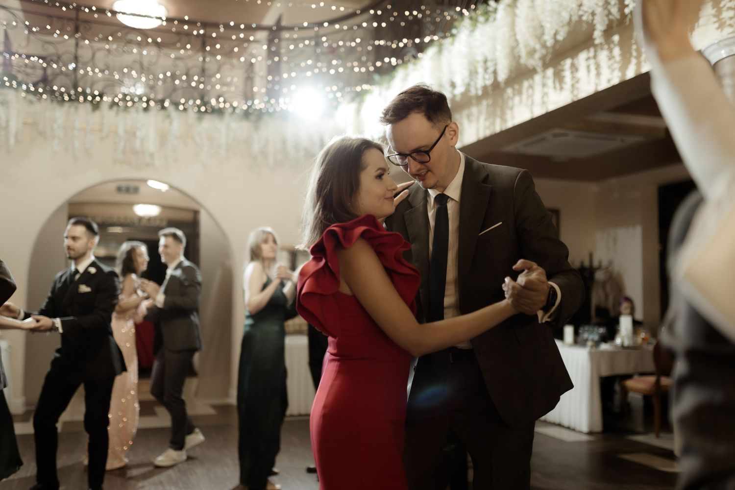 Couple dances elegantly at an indoor wedding reception with woman in red dress and man in dark suit under soft lighting.