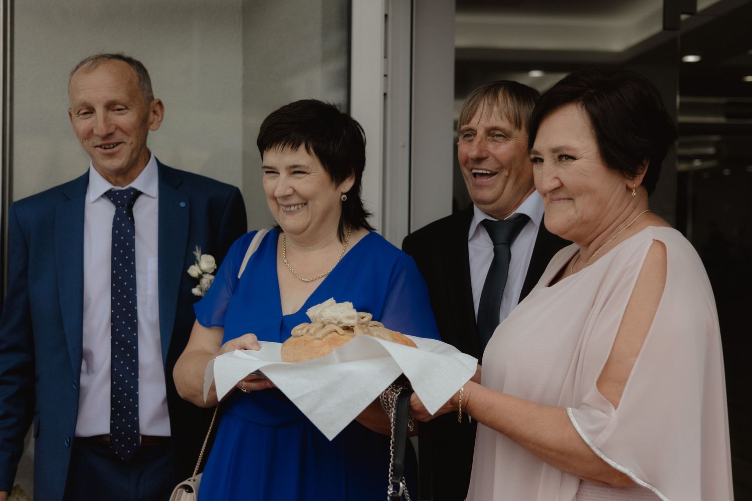 A group of formally dressed people smile together at a social gathering, with someone holding a white cloth or document.