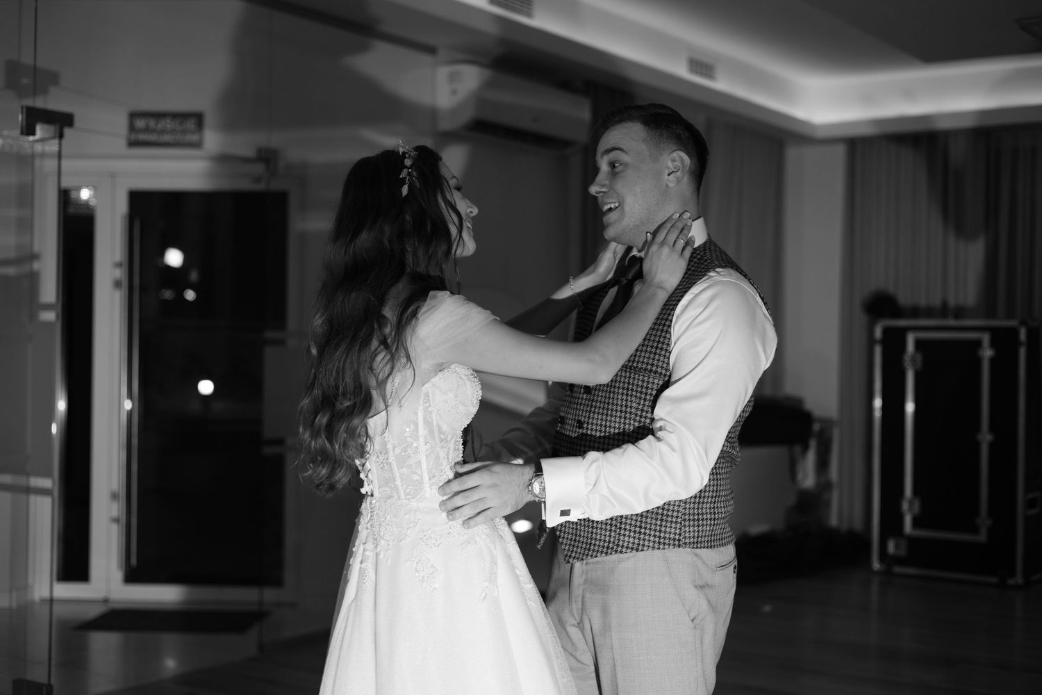 A couple shares their first dance at a wedding reception in an elegantly decorated ballroom, captured in black and white.