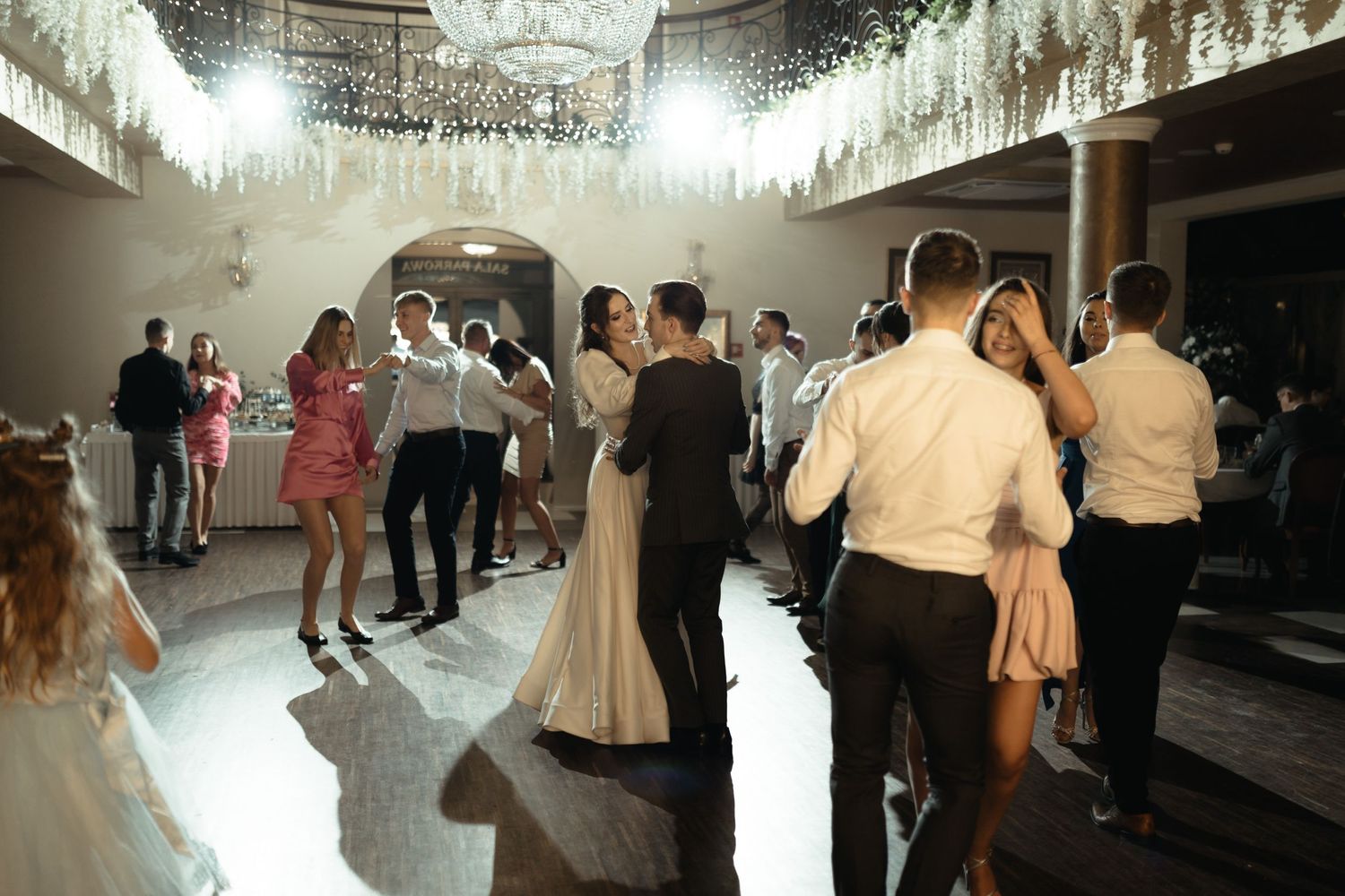 Couples dance together under sparkling crystal chandeliers at an elegant wedding reception venue.