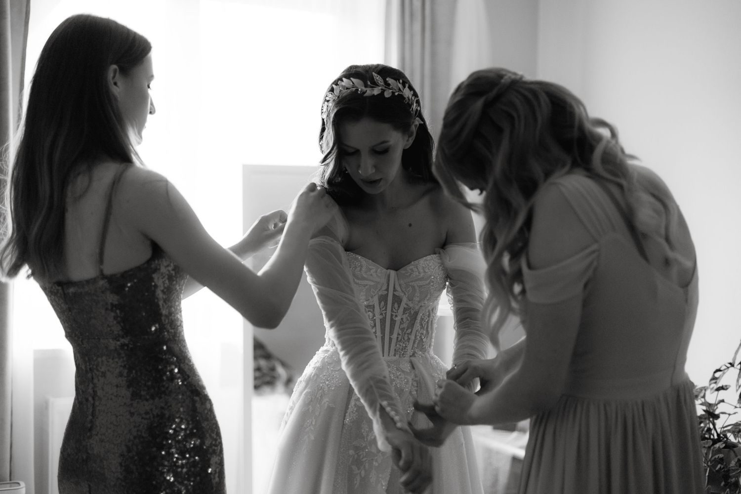 A black and white photo shows women helping another in a white corset dress prepare for a formal event.