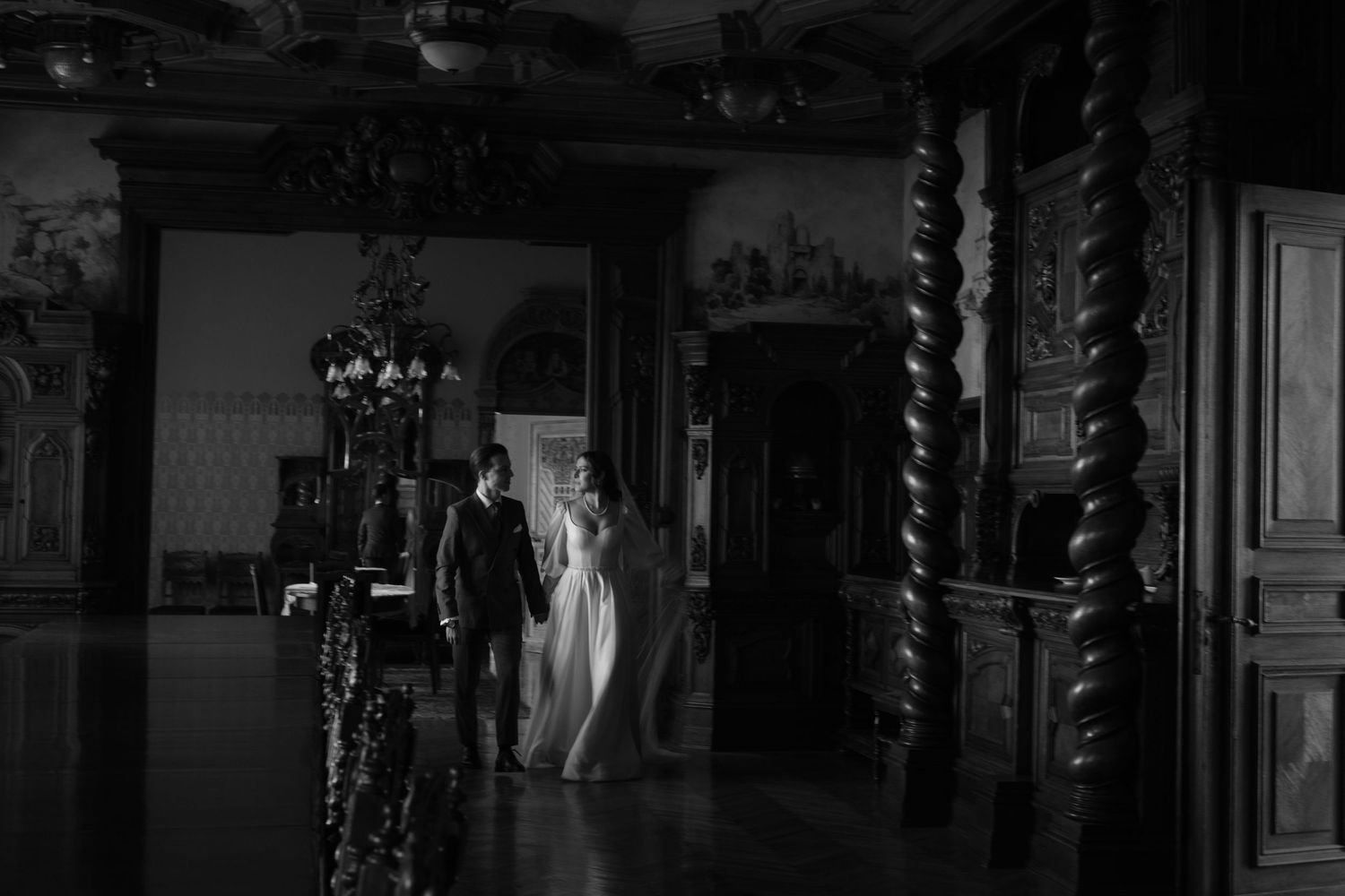 A ghostly figure in white appears in a dark, ornate hallway with carved wooden columns and antique decor.