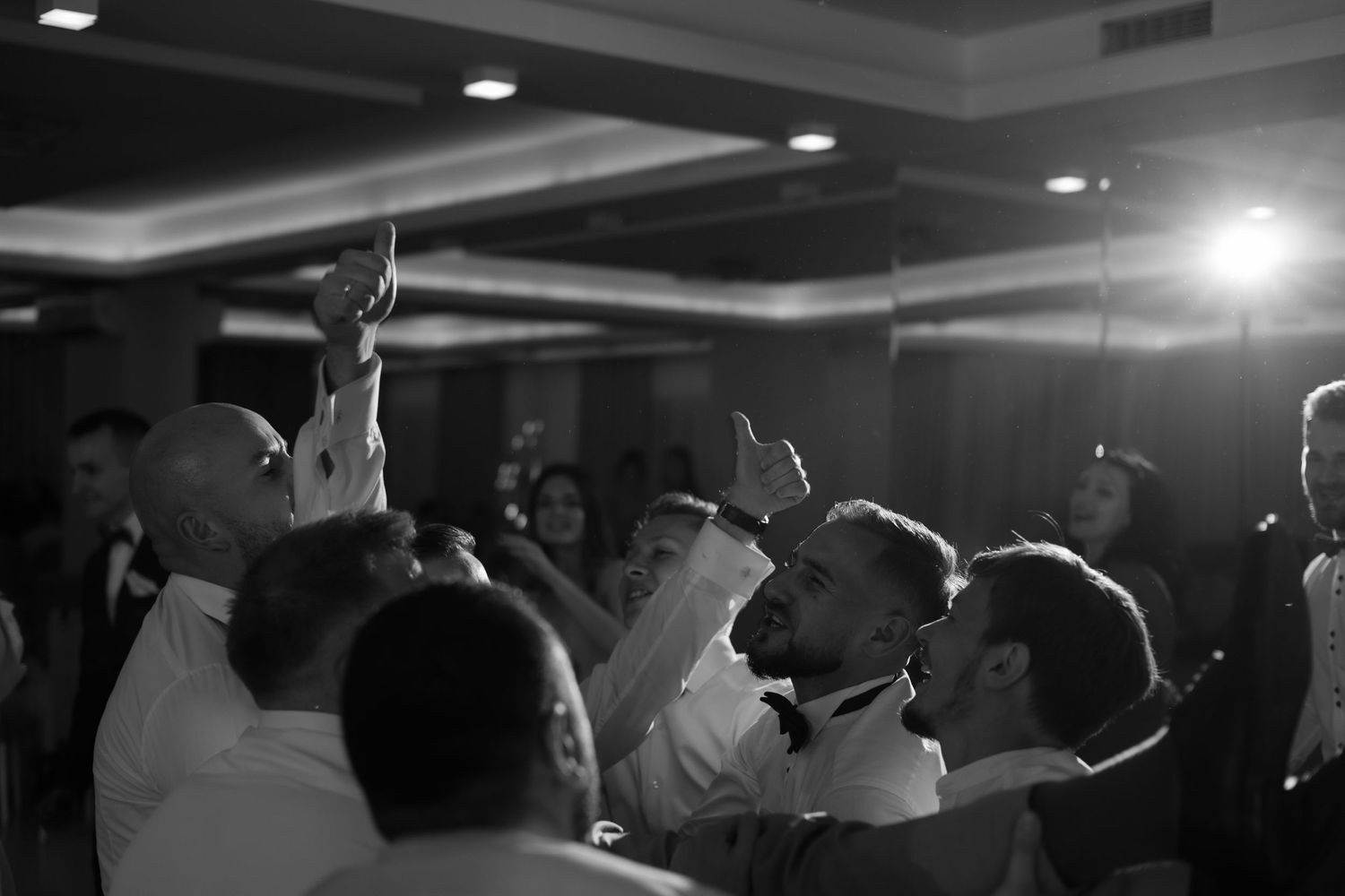 Black and white photo of people dancing with raised hands at what appears to be a wedding reception or party.