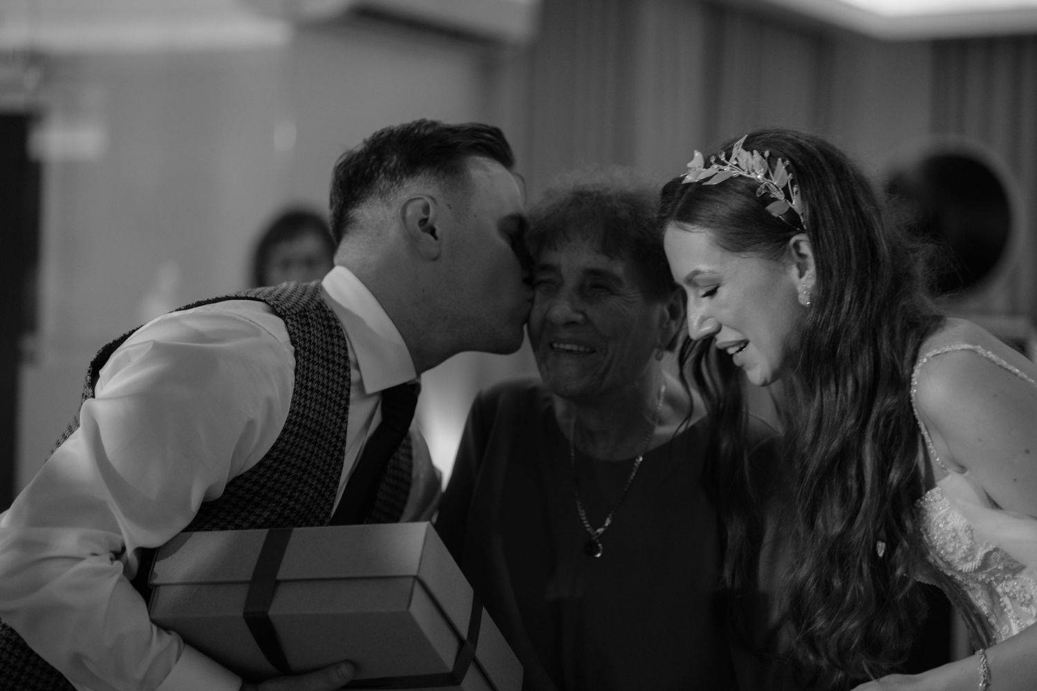 A joyful moment captured in black and white at a wedding reception as couple interact intimately while others look on.