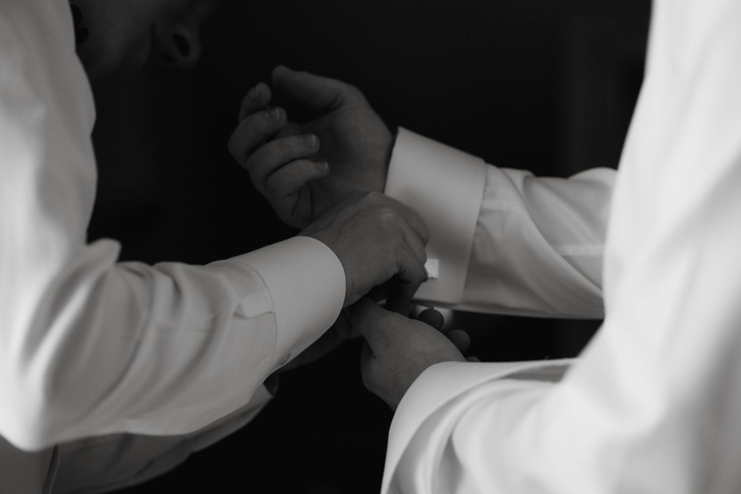 Black and white photograph showing hands adjusting formal shirt cuffs in an elegant dressing moment.