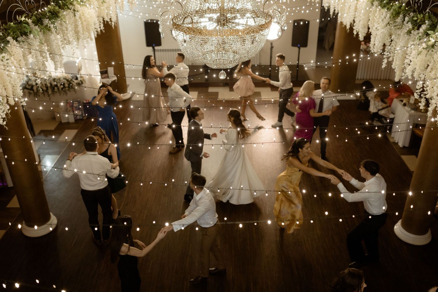 Couples dance together in an elegant ballroom illuminated by twinkling lights and chandeliers at an evening reception.