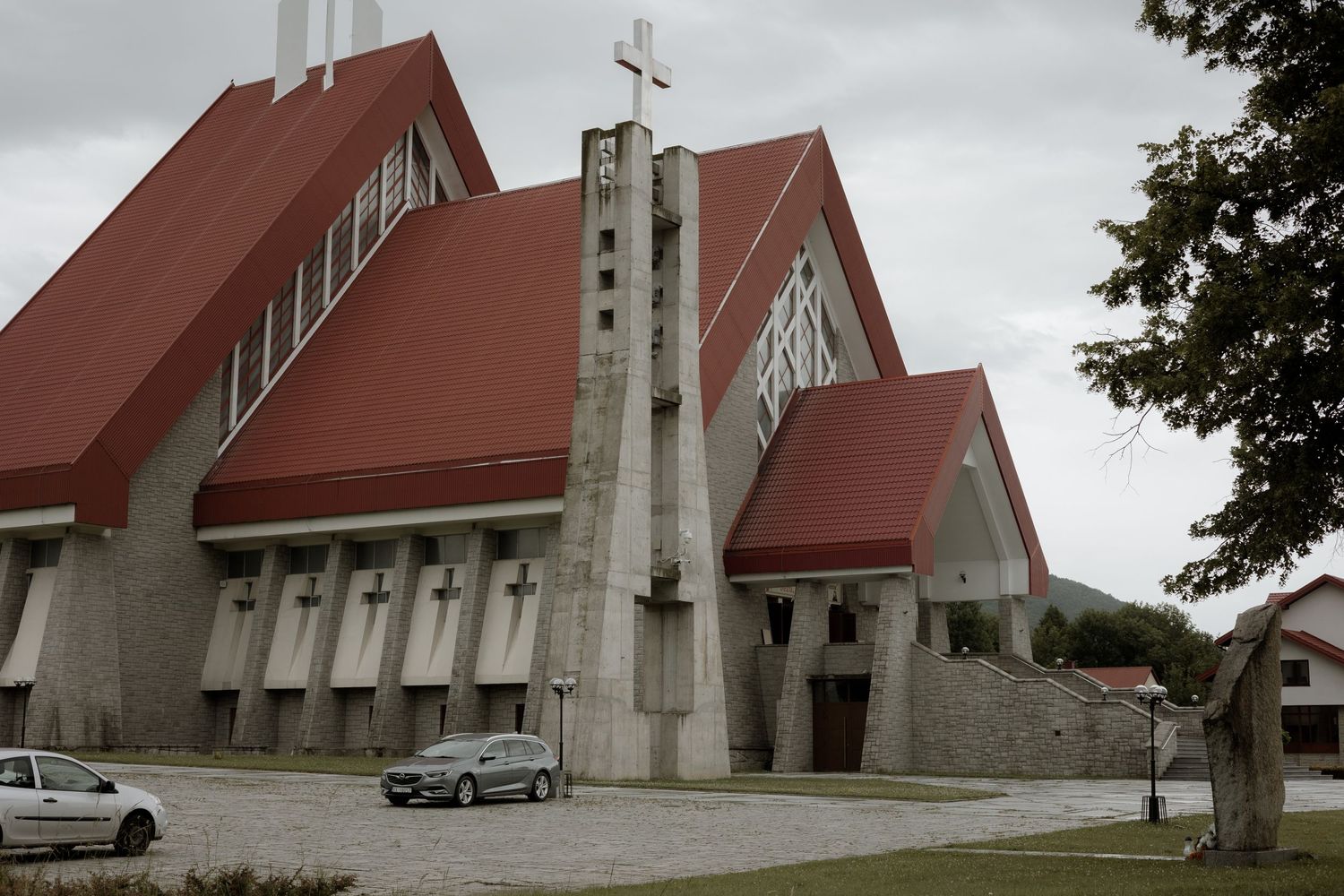 Modern church building with dramatic angular red roof and tall concrete tower featuring a cross on top.