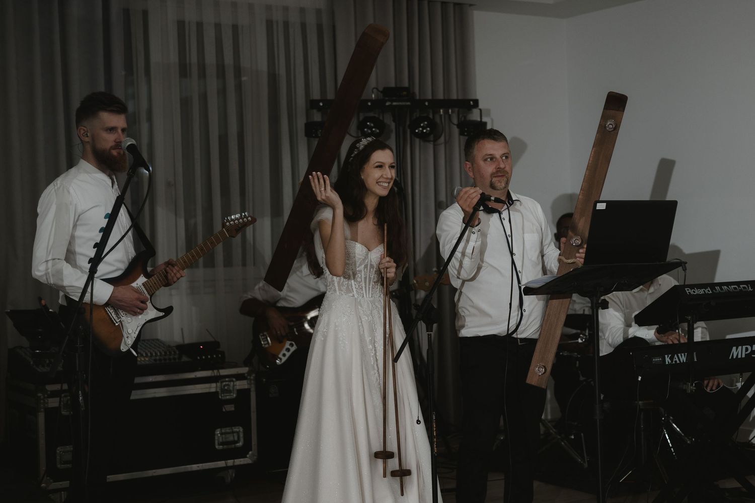A live band performs at a wedding reception with musicians on guitar and a singer in a white bridal gown.