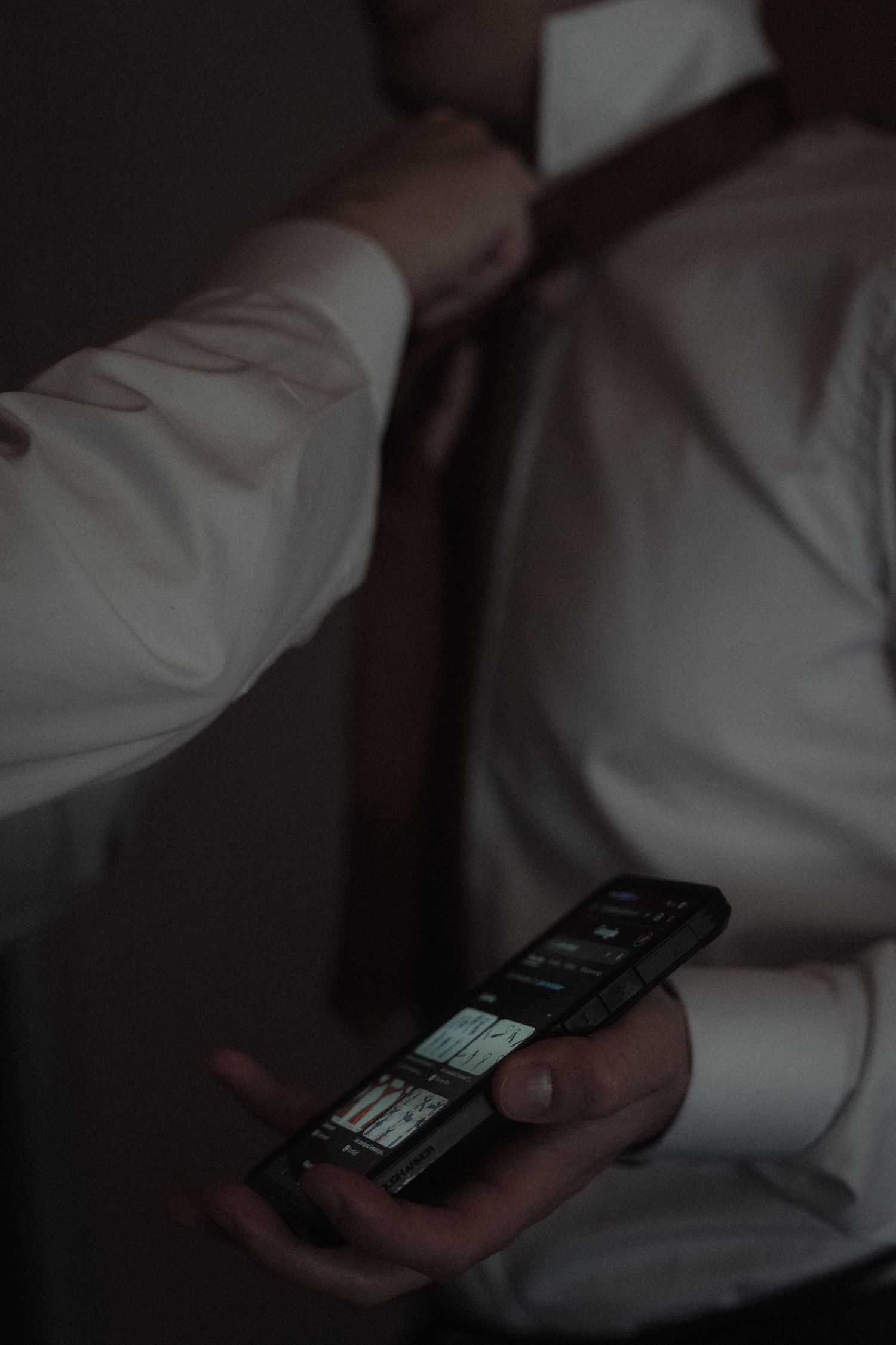Person in white shirt holding an old flip phone in dimly lit setting.
