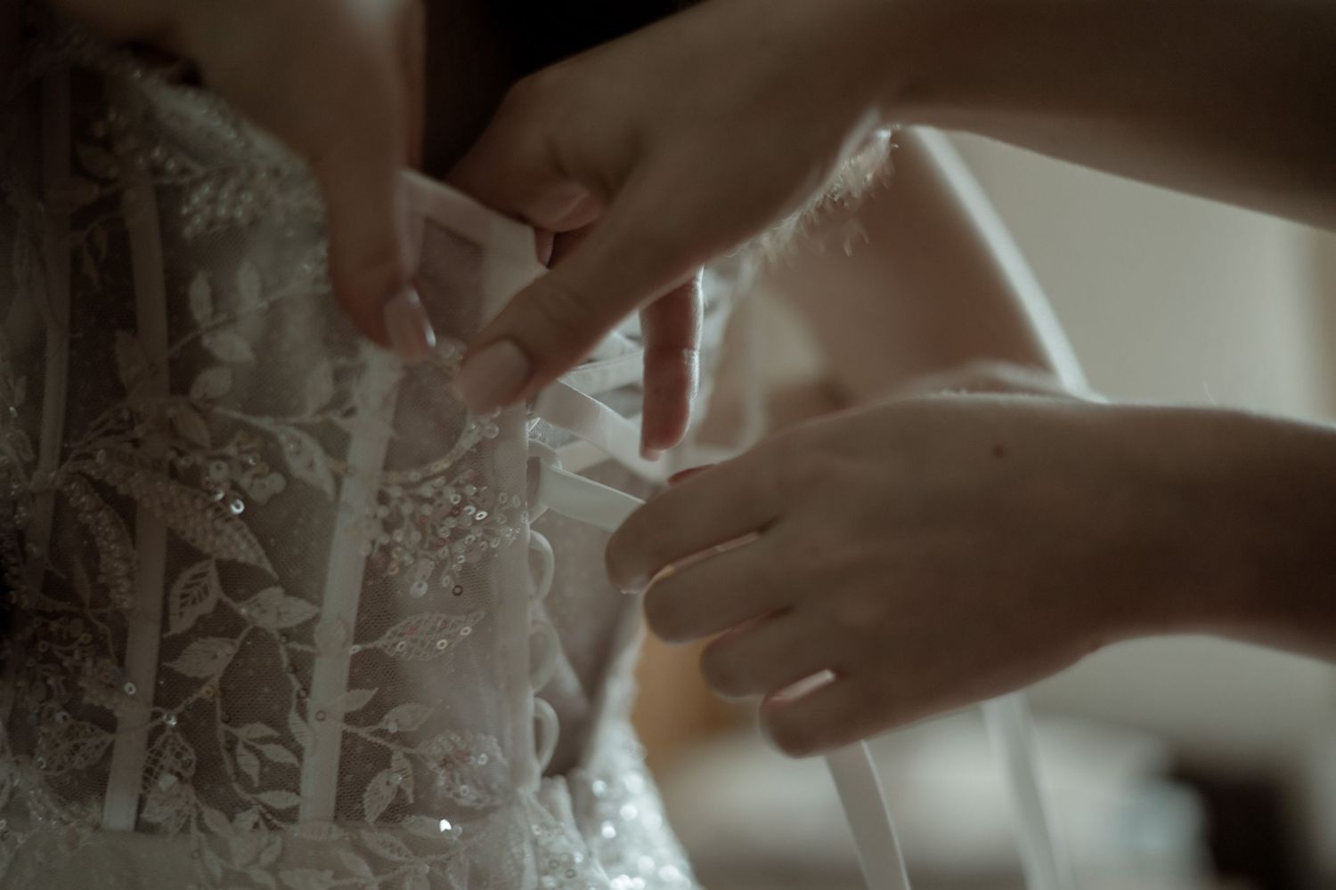Close-up view of hands adjusting delicate white lace details on a wedding dress.