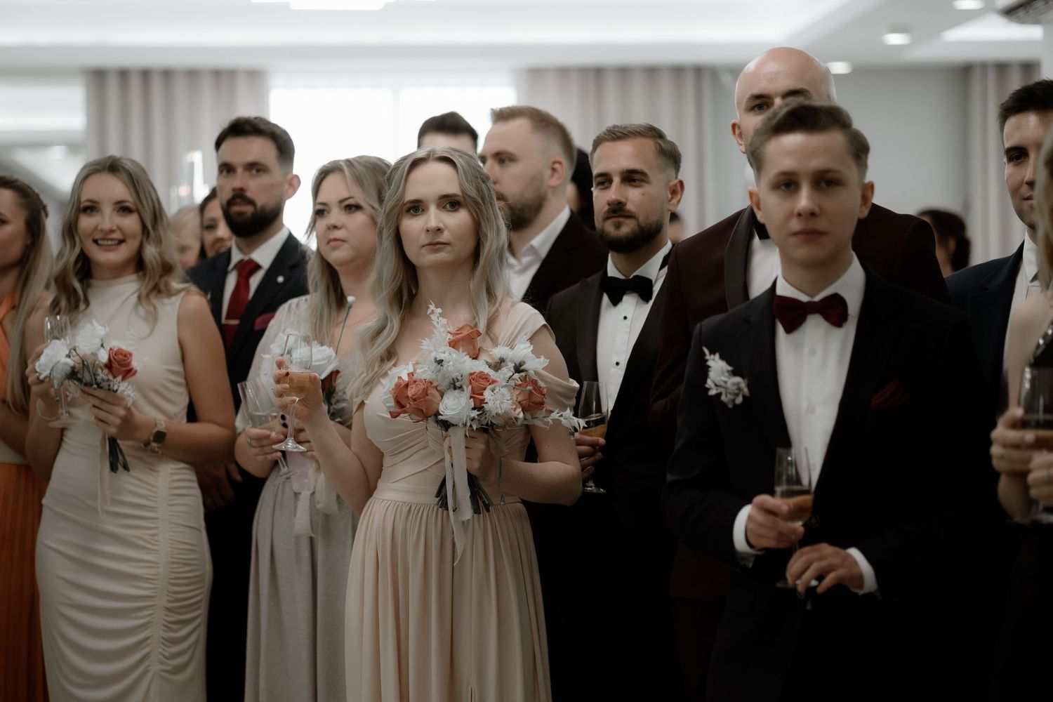 Wedding party members in formal attire hold champagne glasses during an elegant indoor celebration.