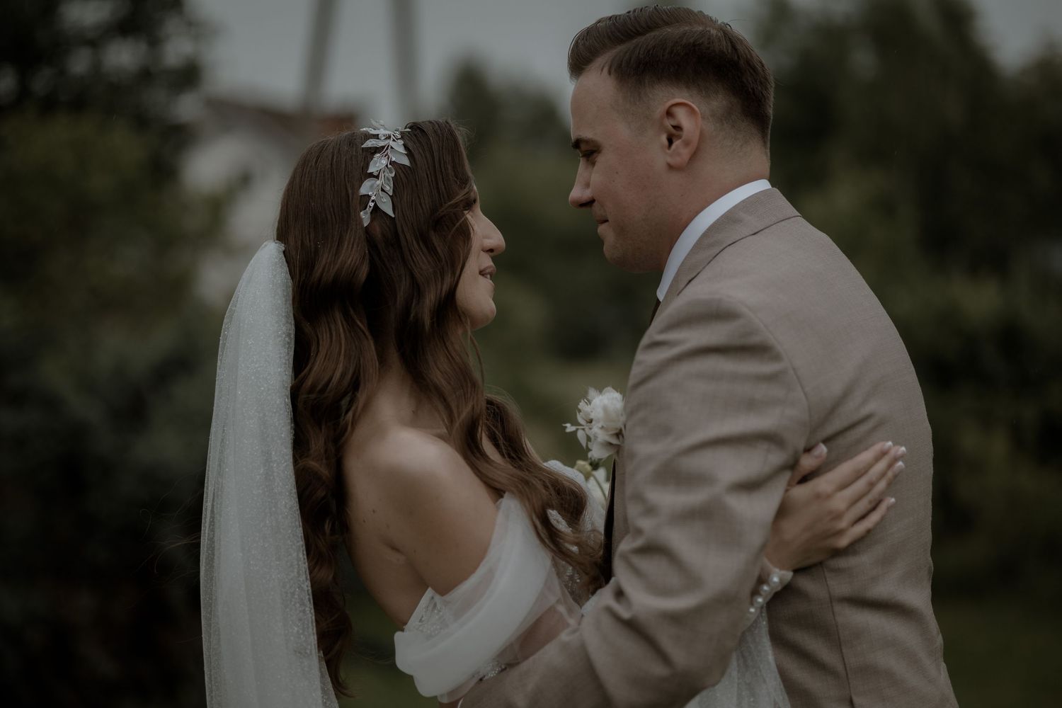 A couple in wedding attire share an intimate moment outdoors with a moody and romantic atmosphere.