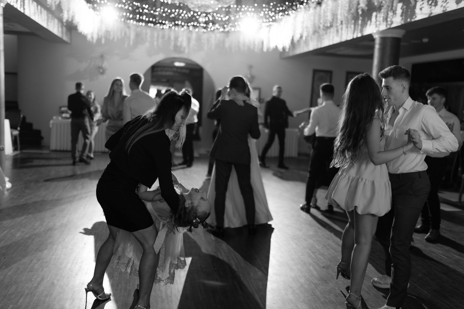 People dancing on a wooden dance floor under decorative lights at a party in black and white photography.