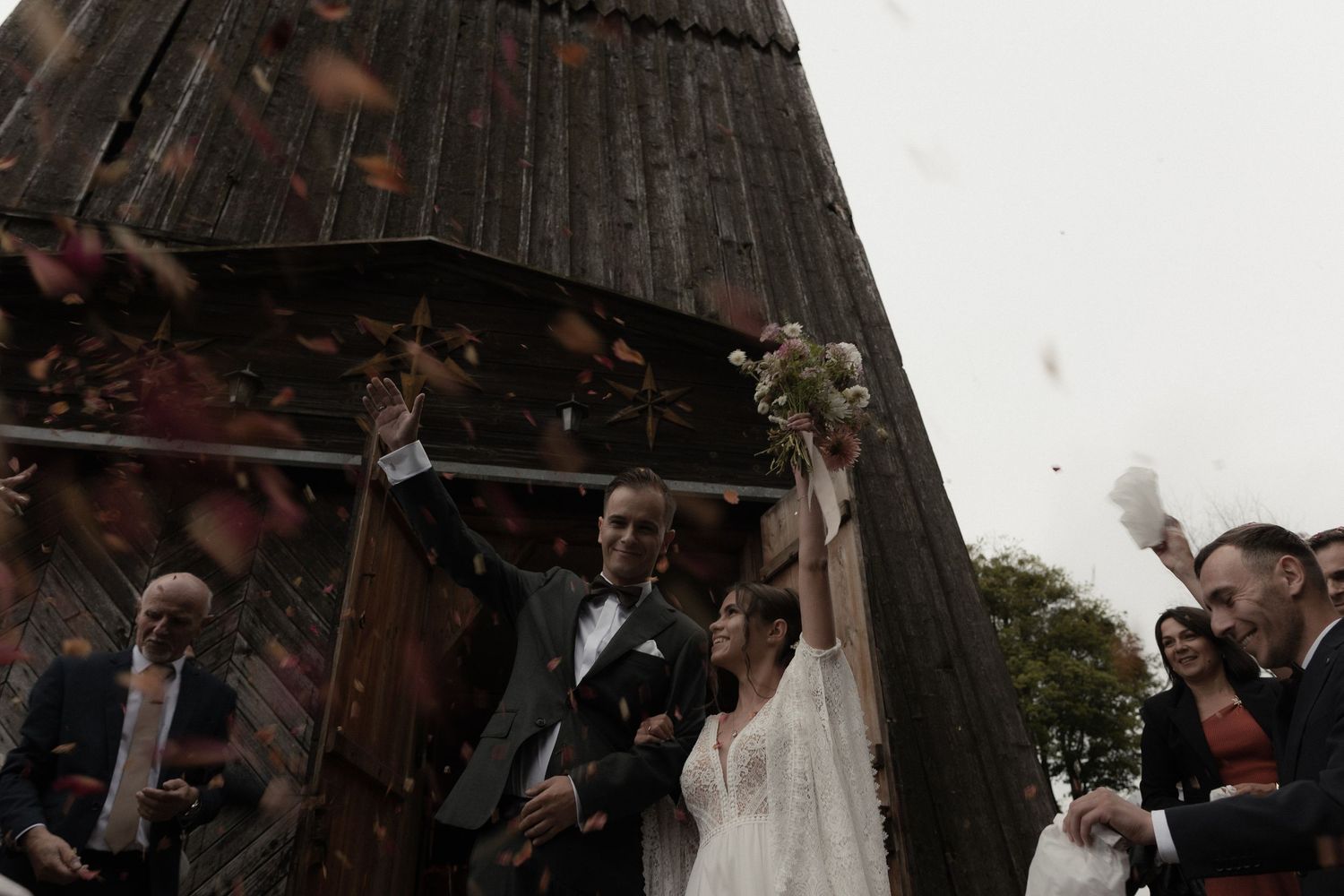 A wedding party poses together in front of a rustic wooden barn door during a celebration.