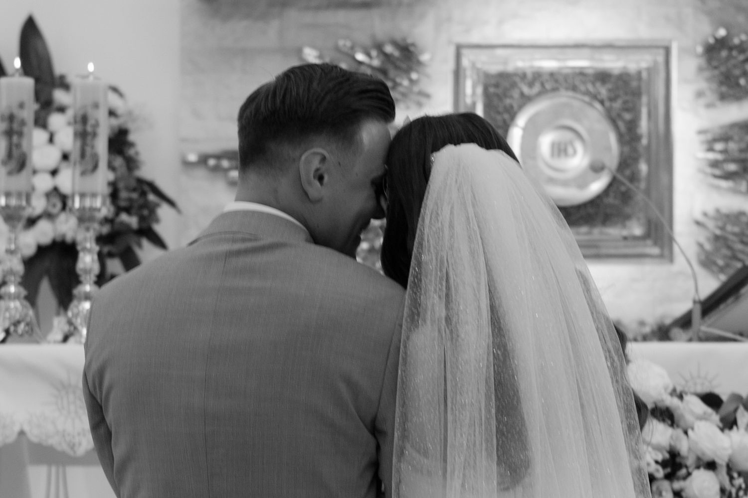 A black and white wedding photograph showing a couple in traditional bridal attire facing away from the camera.