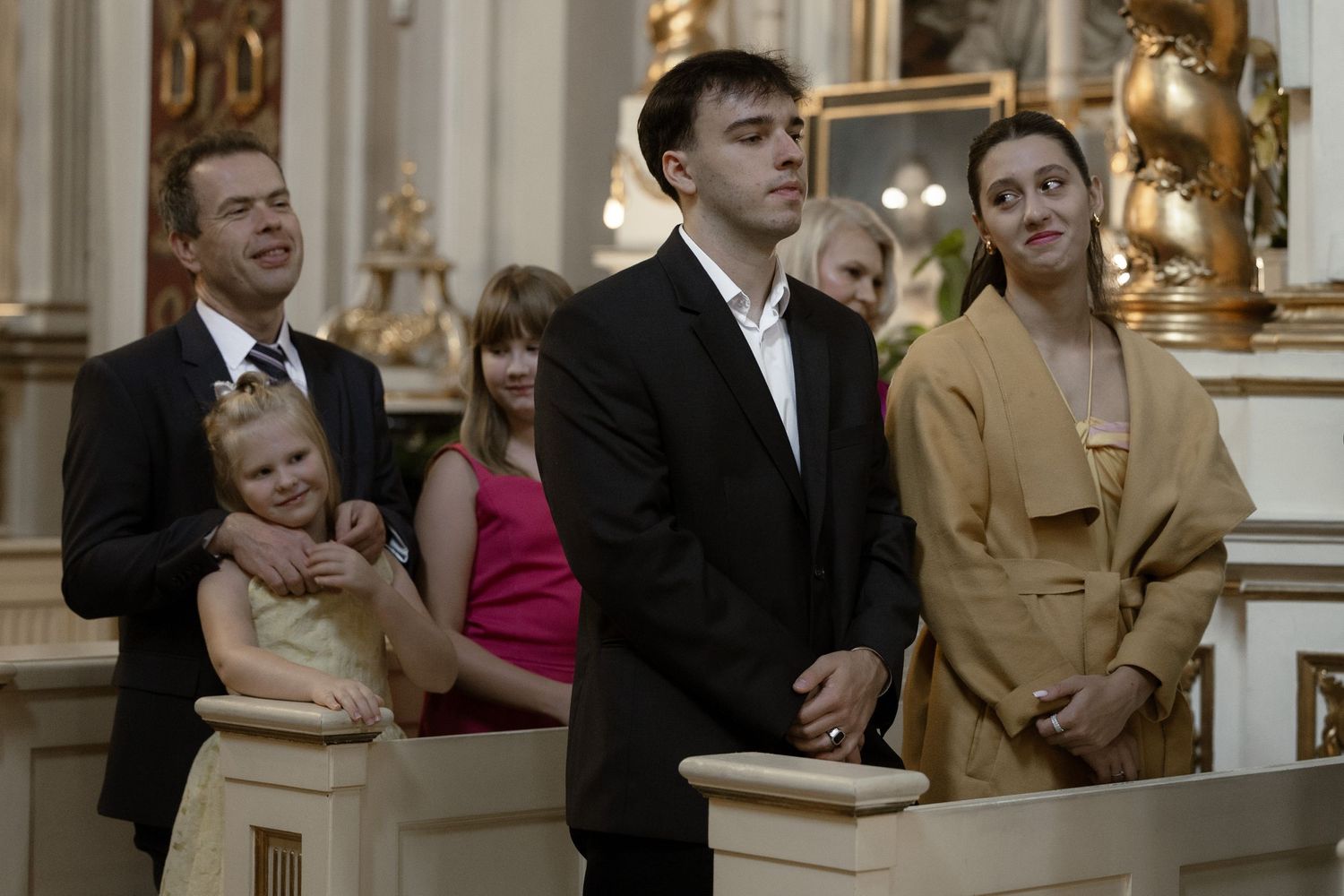 Group of formal wedding attendees stand in a traditional church pew during a ceremony.