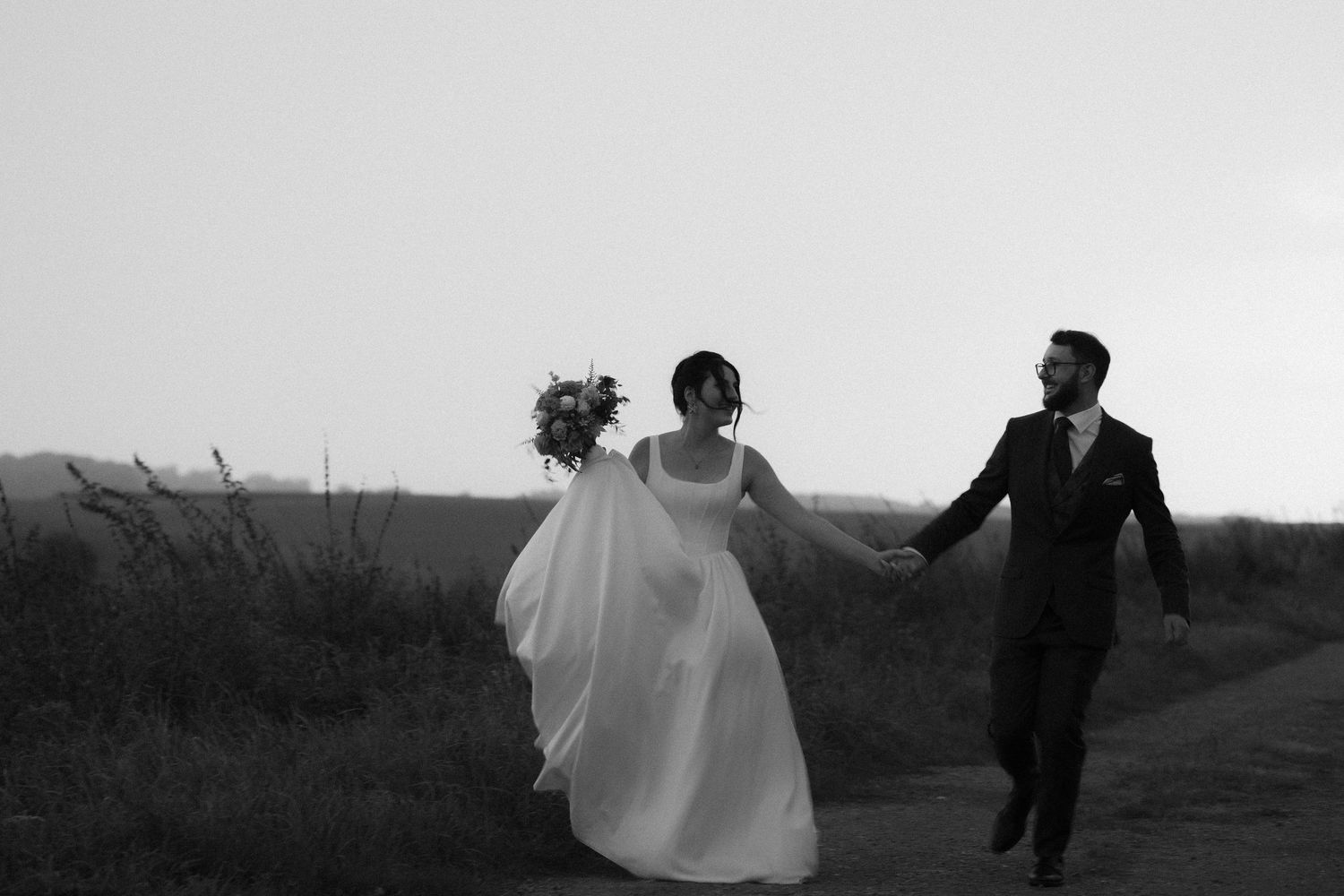 A series of romantic silhouettes show a couple dancing and embracing in a field at sunset with a flowing wedding dress.