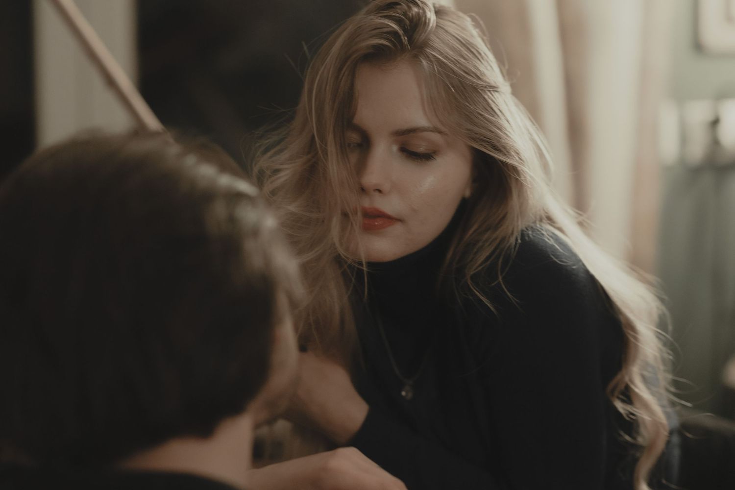 A soft, intimate portrait in muted tones shows two people in a close conversation by natural window light.