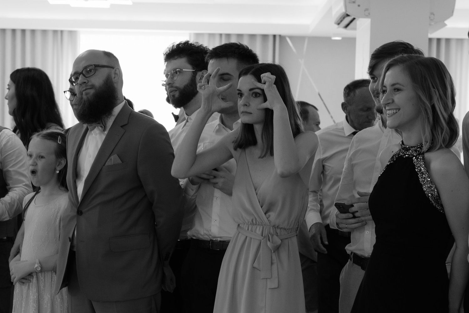 A black and white photograph of a group of wedding guests smiling and watching something off camera at a celebration.