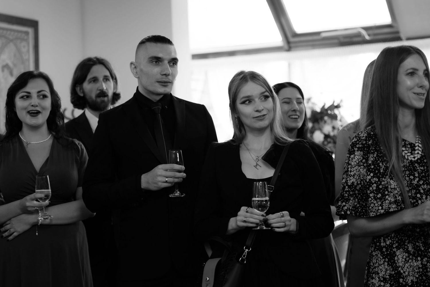 Black and white photo of a group of people at a social gathering holding drinks and standing together.