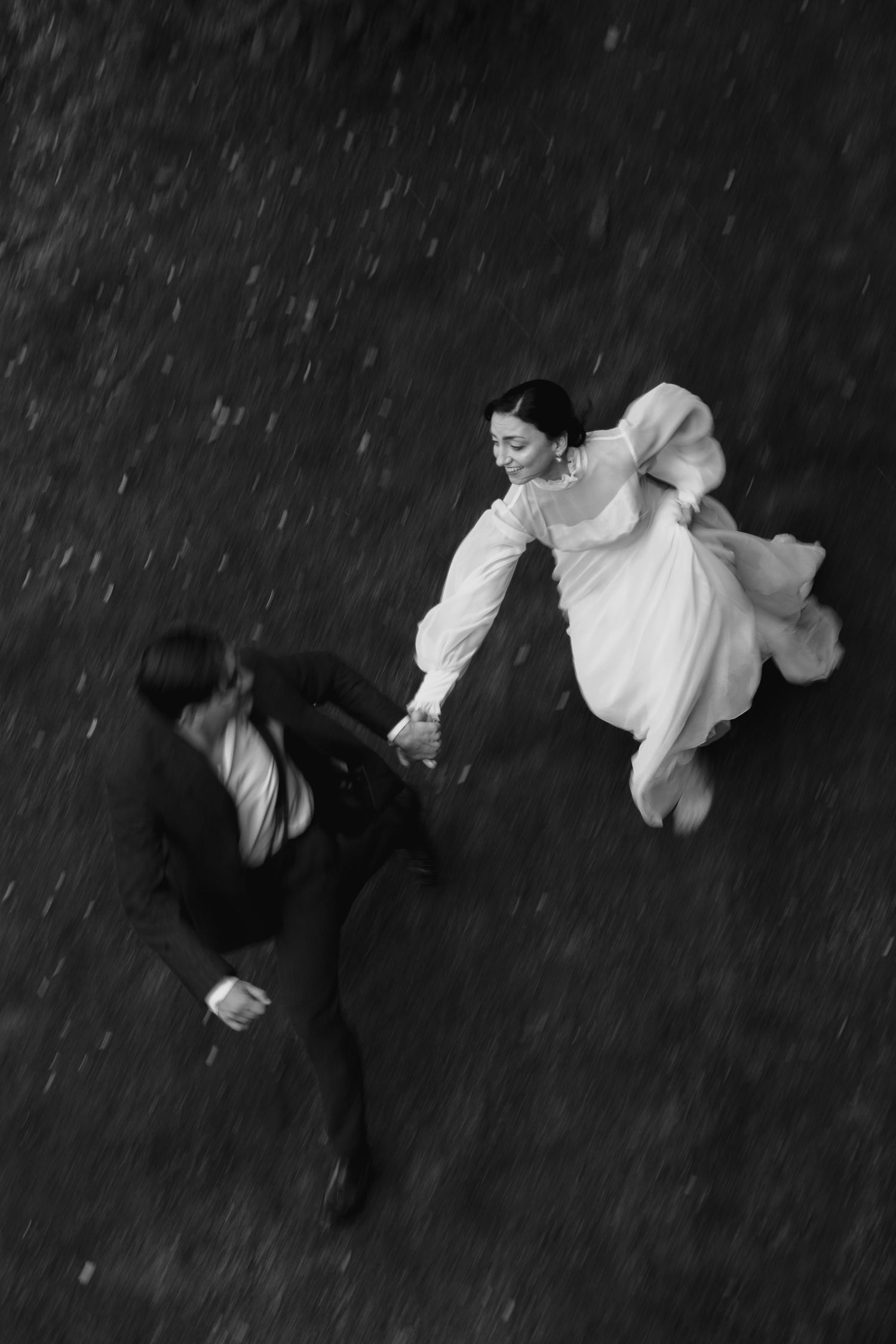 A black and white aerial view of a couple dancing in formal attire, with the woman's white dress flowing against a dark background.