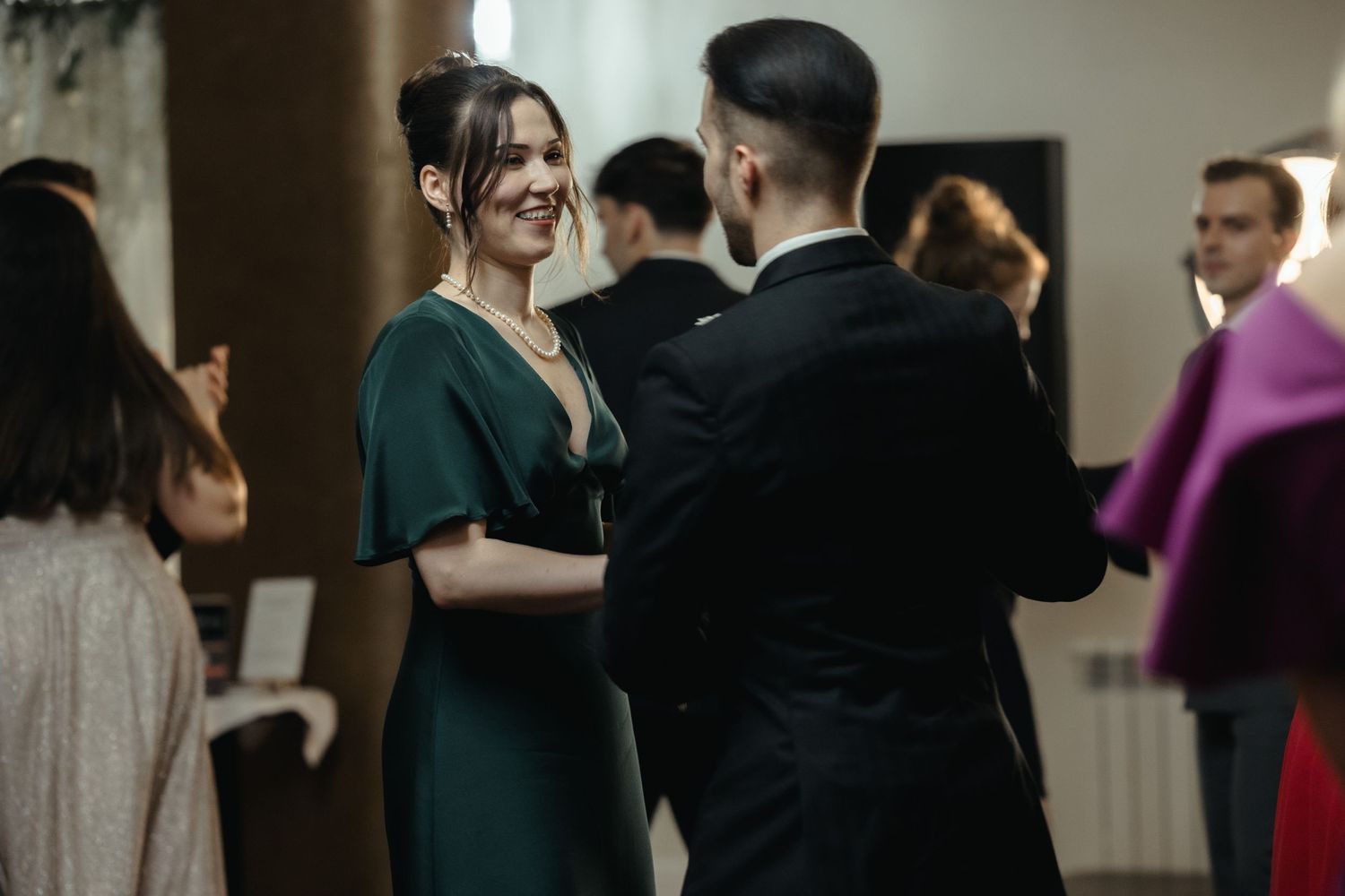 A couple dances together at an elegant event, with the woman wearing an emerald green dress and the man in a black suit.