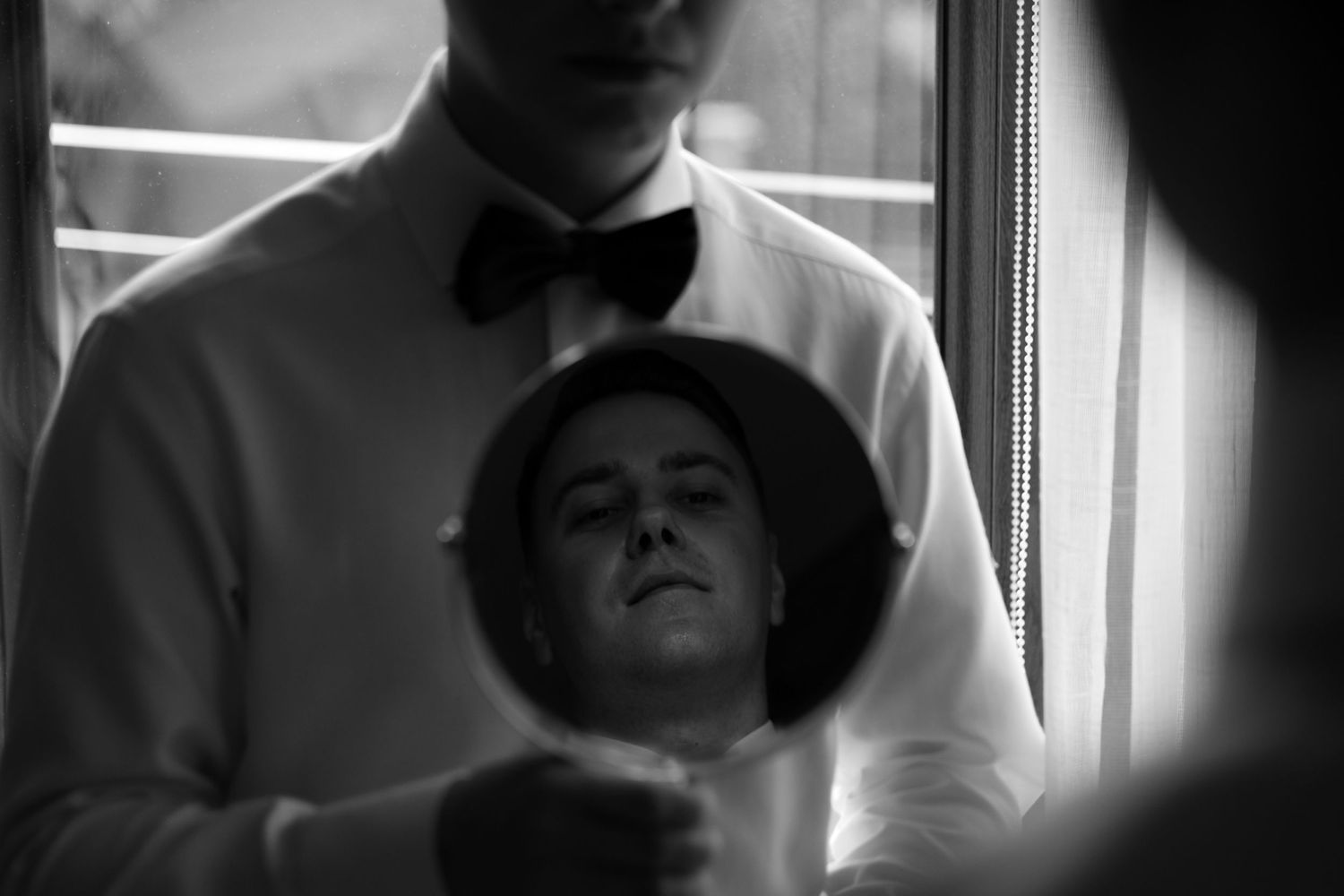 Vintage black and white photograph showing a circular mirror reflection with someone wearing formal attire.