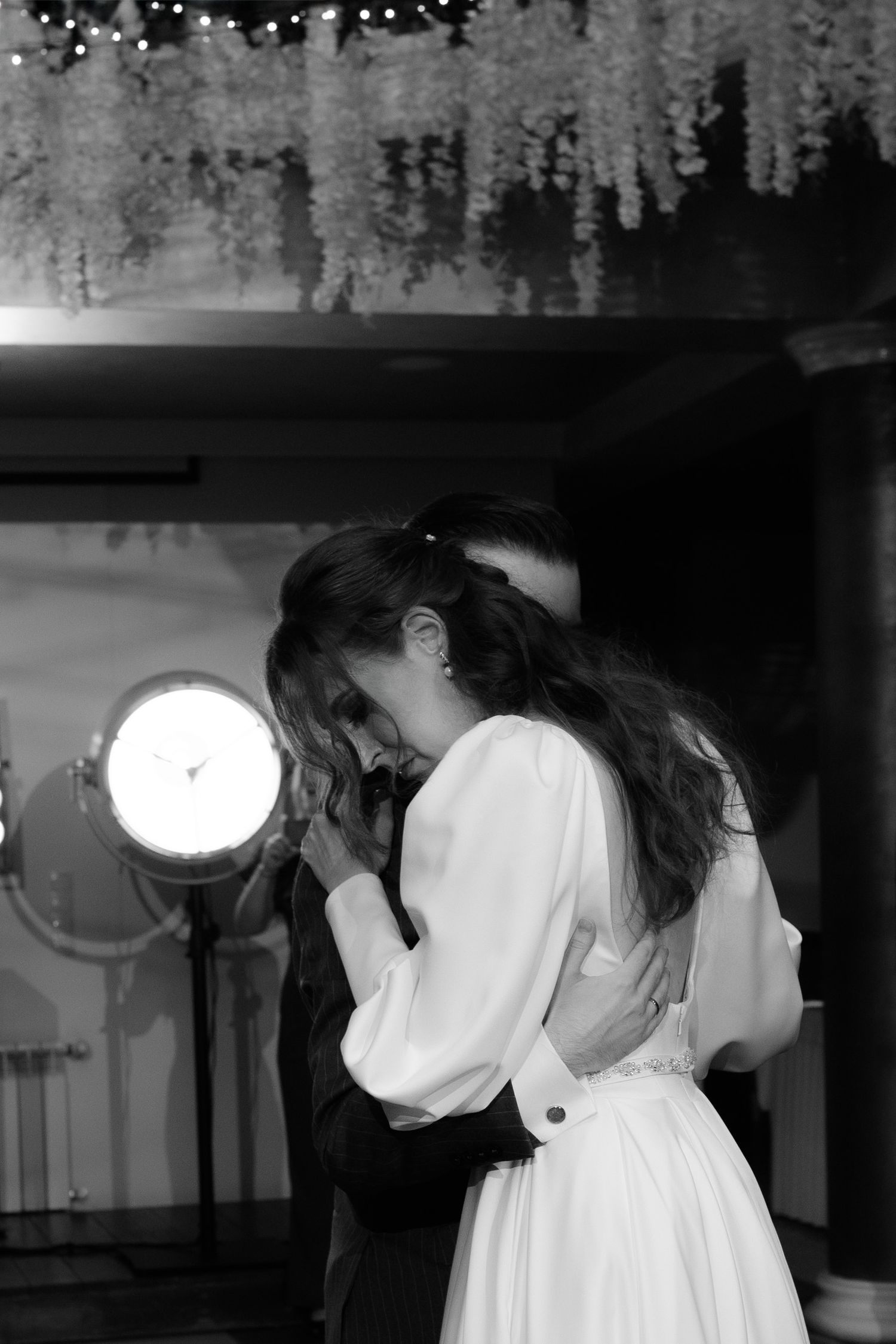 A tender moment between two people dancing in black and white, with one wearing a white flowing dress under dramatic lighting.