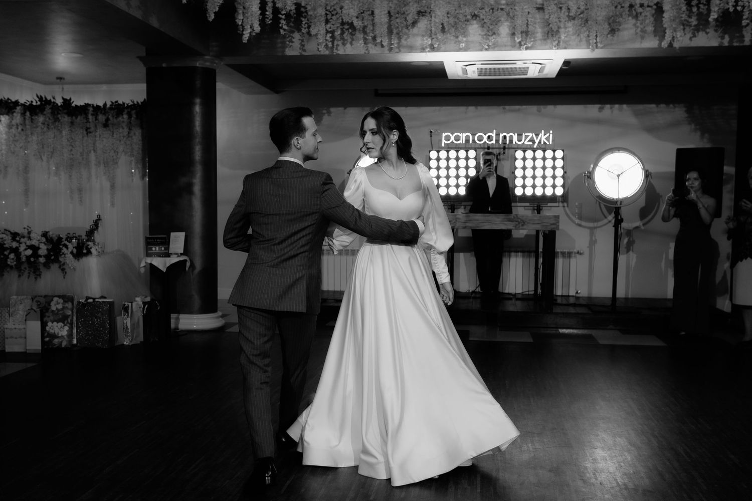 A couple shares their first dance together in black and white at their wedding reception on a dark dance floor.