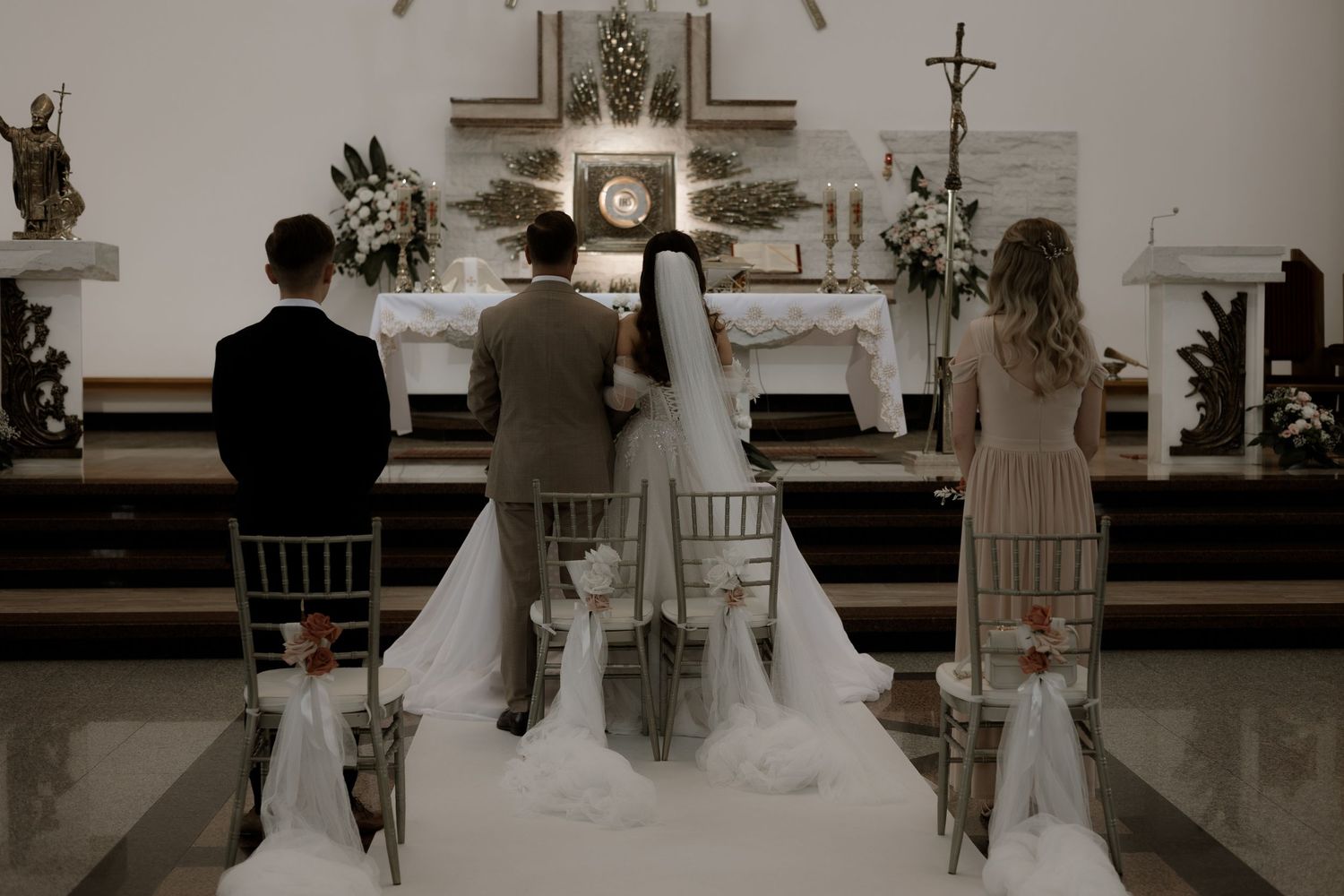Wedding ceremony taking place at a church altar with bride and groom kneeling before a priest.