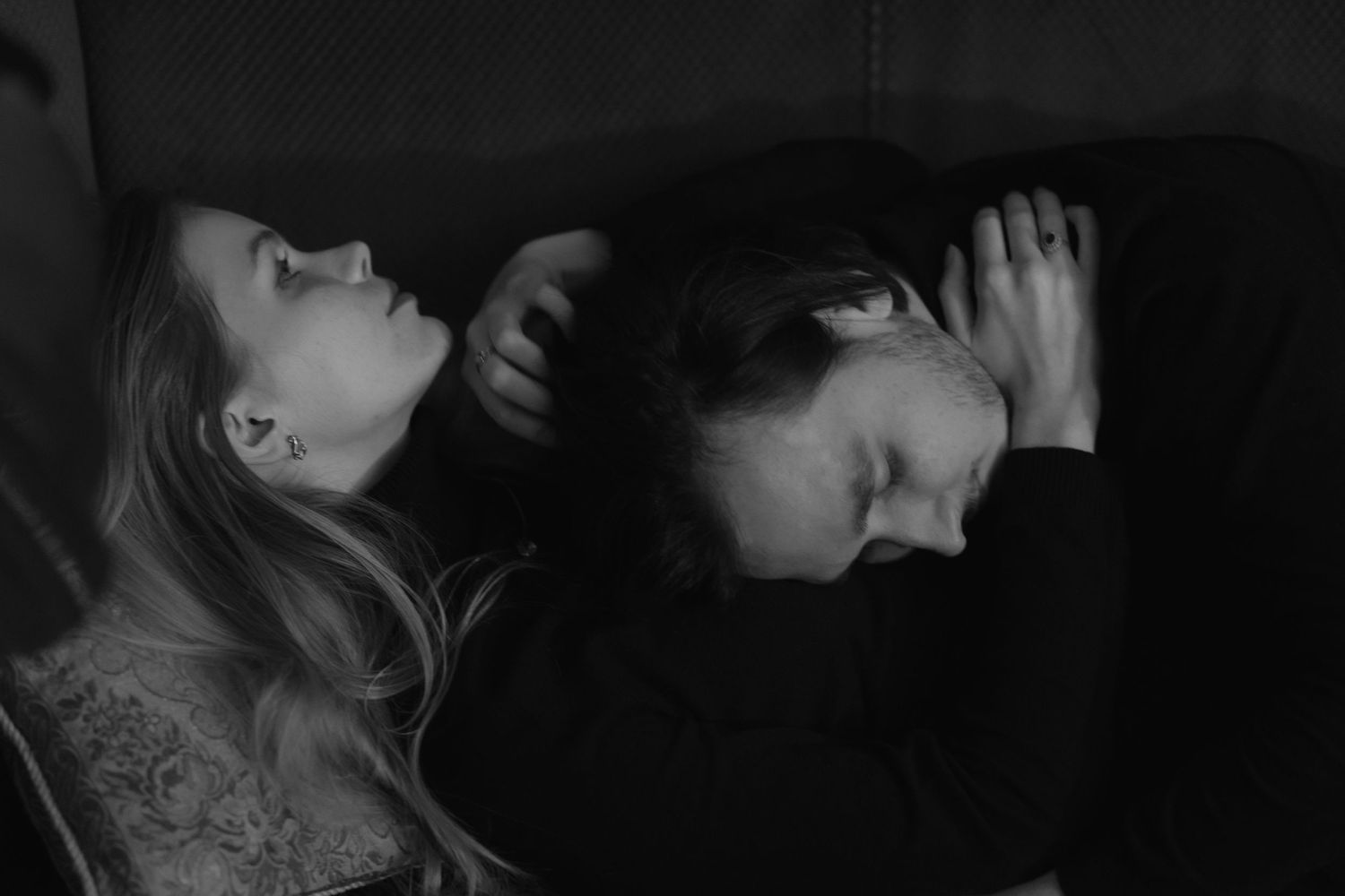 Black and white artistic photograph showing two people with contrasting expressions lying down in dramatic lighting.