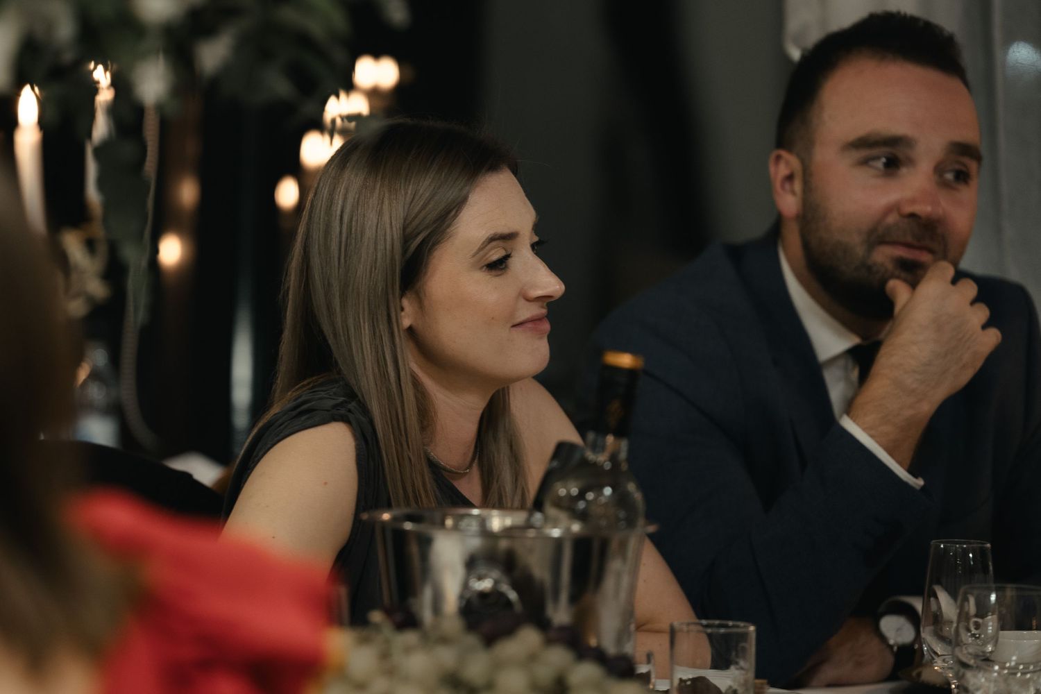 A couple appears to be listening intently during a candlelit dinner in a dimly lit restaurant.