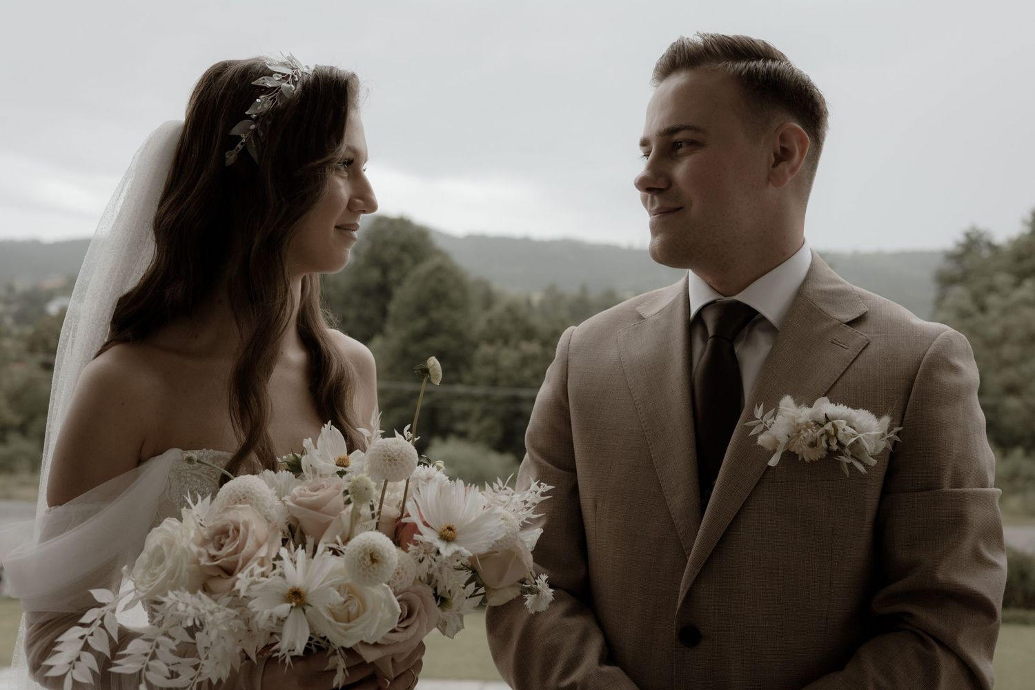 A bride and groom share an intimate moment while posing outdoors, with the bride holding a pink and white bouquet.