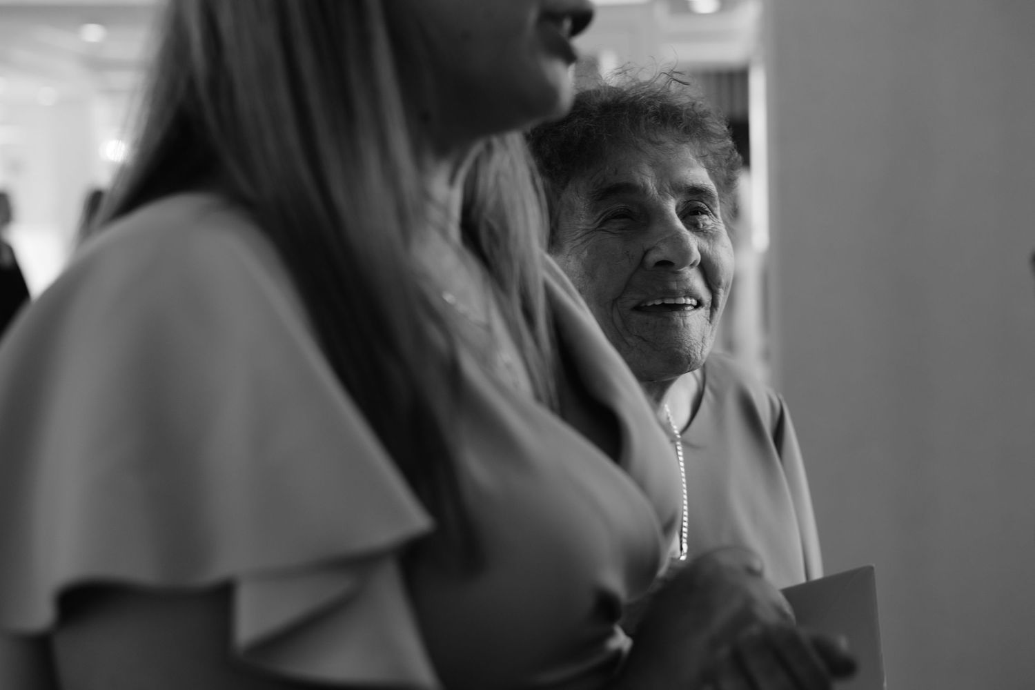 Black and white candid shot shows warm interaction between two people in conversation captured from a close angle.
