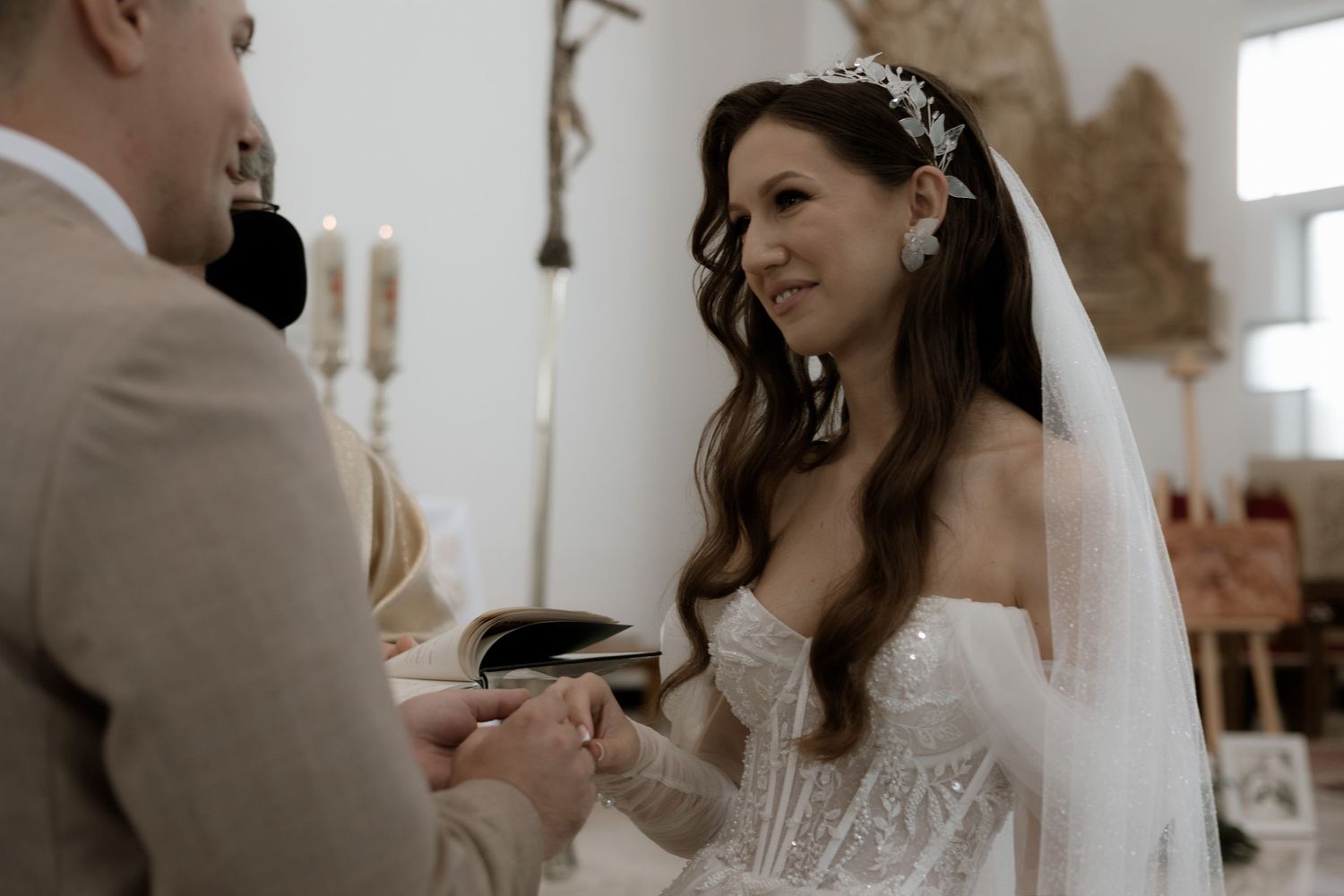 A wedding ceremony taking place indoors with the bride wearing an elegant strapless white dress and veil during the ring exchange.