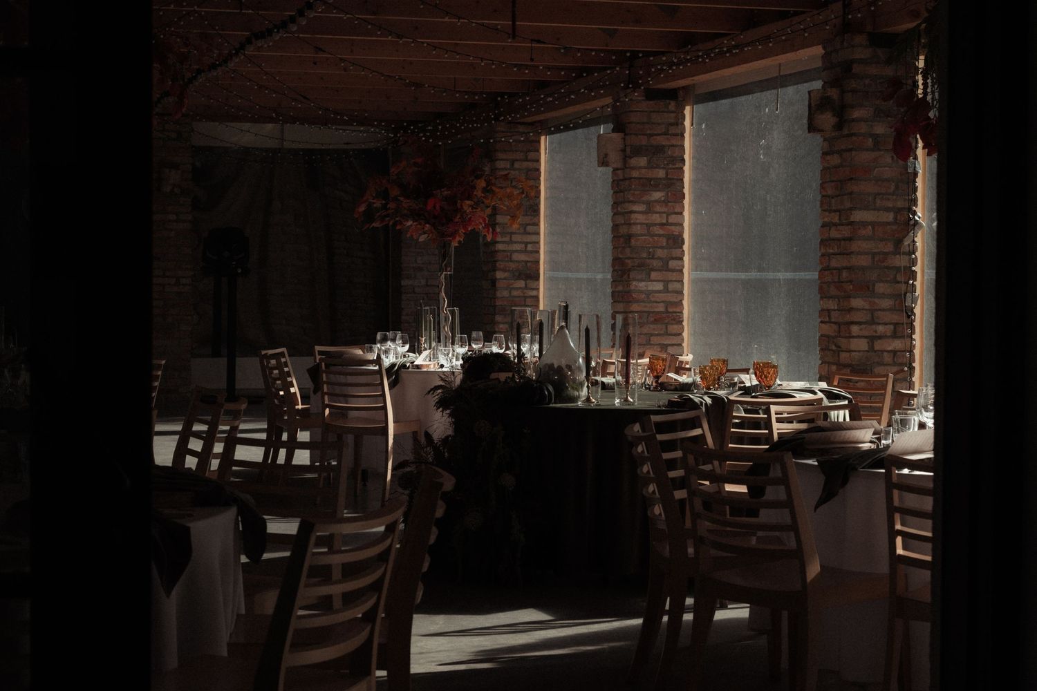 Rustic restaurant interior with exposed brick walls, wooden tables and chairs in warm ambient lighting.