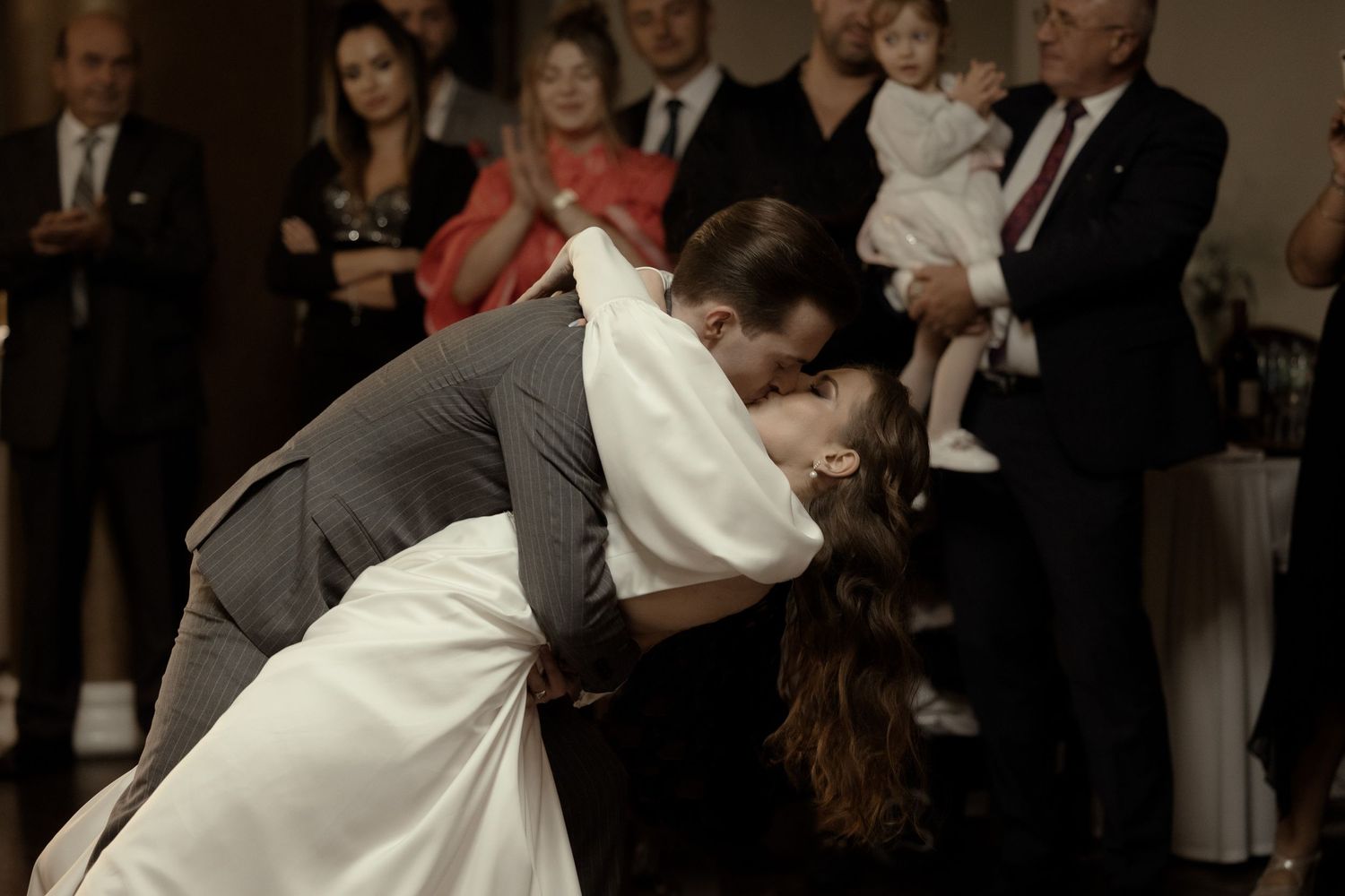 A groom dips his bride on the dance floor during their wedding reception as guests look on in the background.