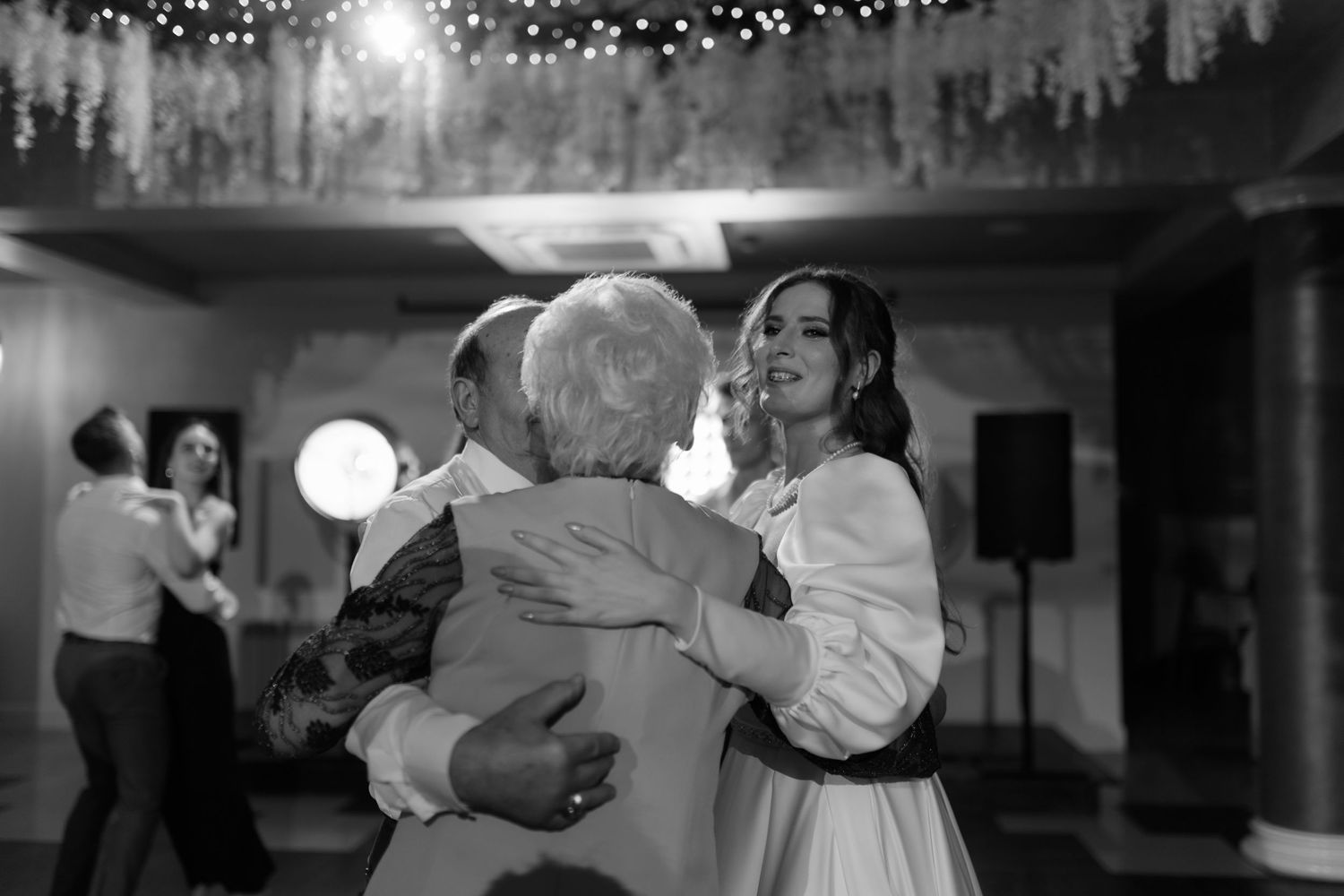 A tender moment on the dance floor at a wedding reception with soft lighting and decorative string lights above.