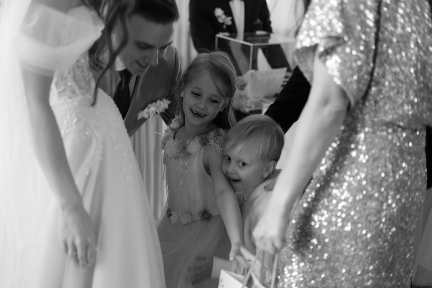 A black and white candid moment showing excited children and elegantly dressed guests at a formal wedding celebration.