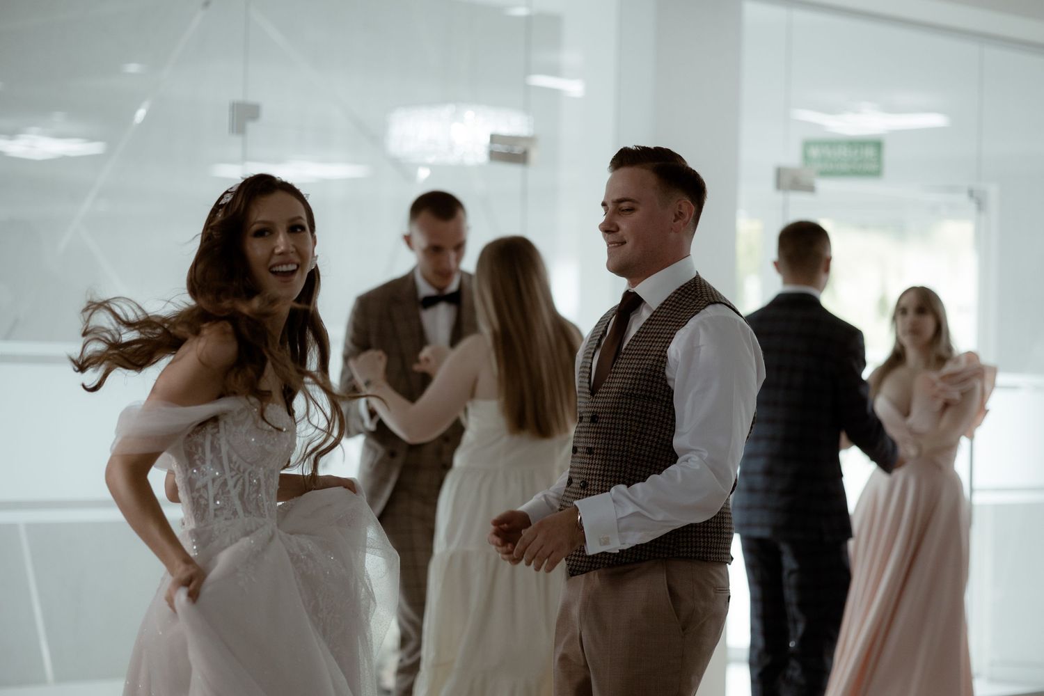 Wedding party guests dancing together on dance floor at a modern venue with white walls.